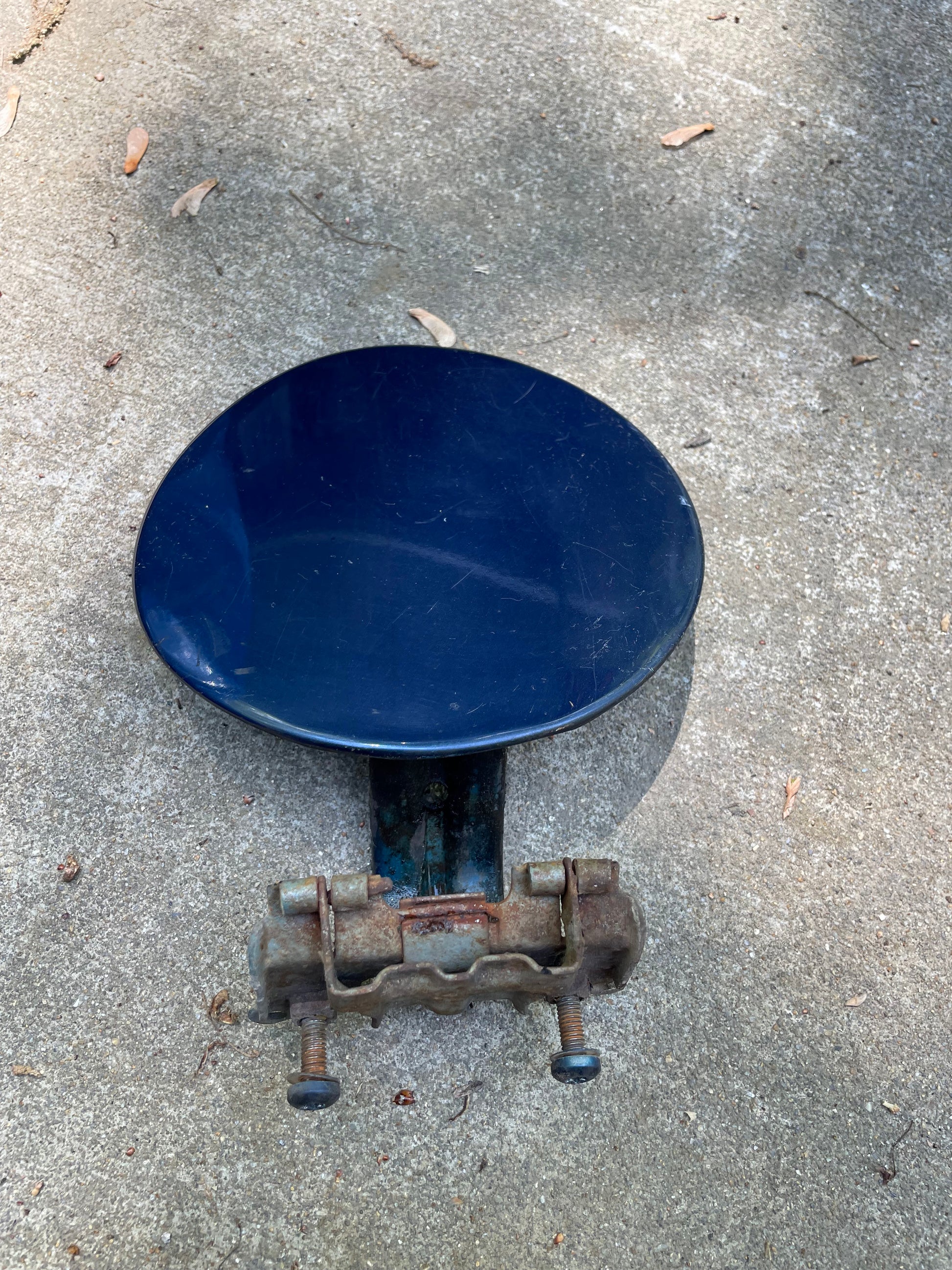 A blue OEM Fuel Filler Neck Door Gas Tank Cover by General Motors for 2001-2004 Chevy S10 & GMC Sonoma, shown on a concrete surface with a rusty clamp and scattered small leaves.
