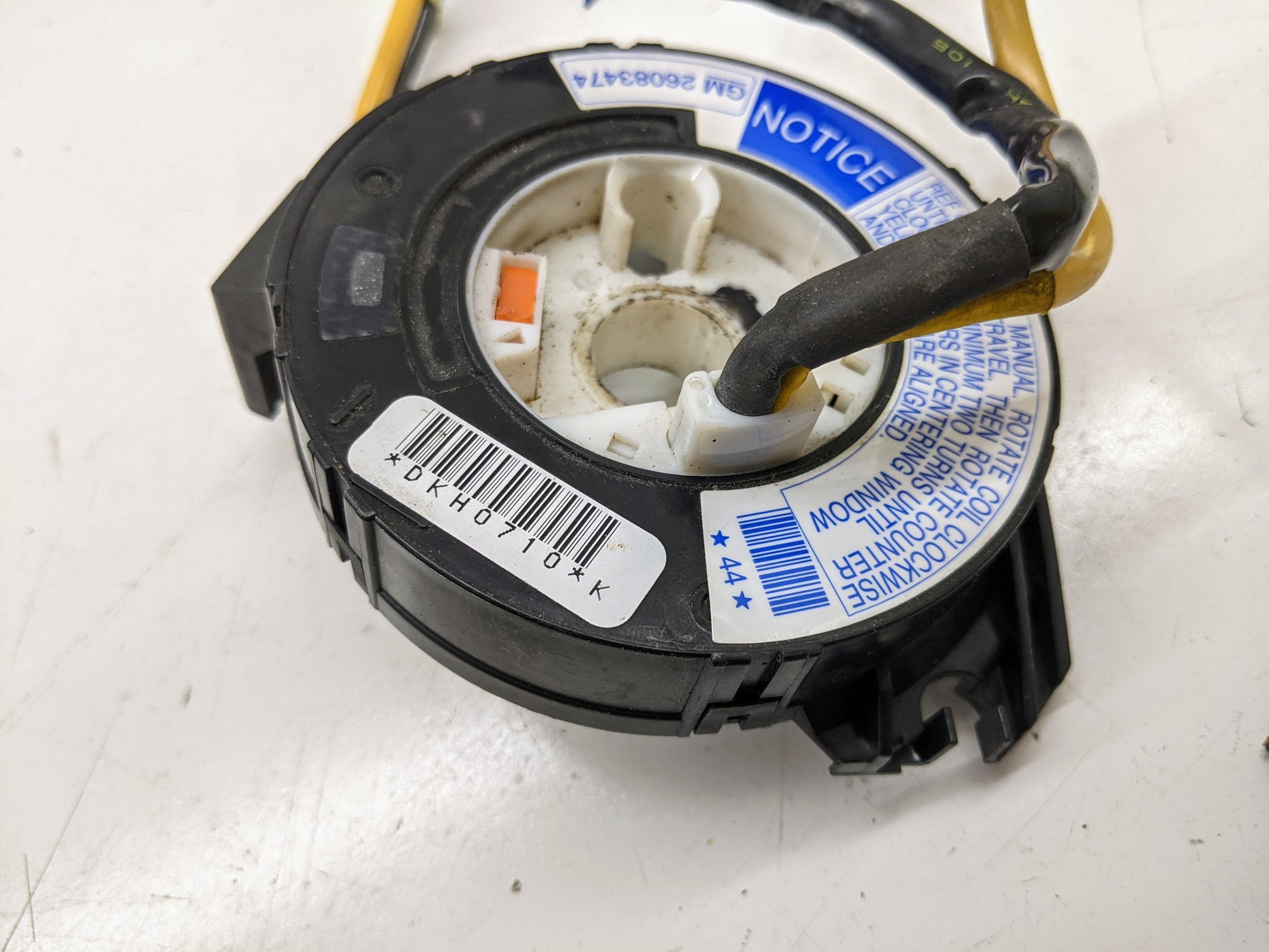 Close-up of a General Motors OEM Steering Wheel SRS Air Bag Clock Spring w/Radio Controls for 2000-2003 Chevy S10 Blazer, featuring barcode, labels, warning notice, wires, and circular center on a white surface.