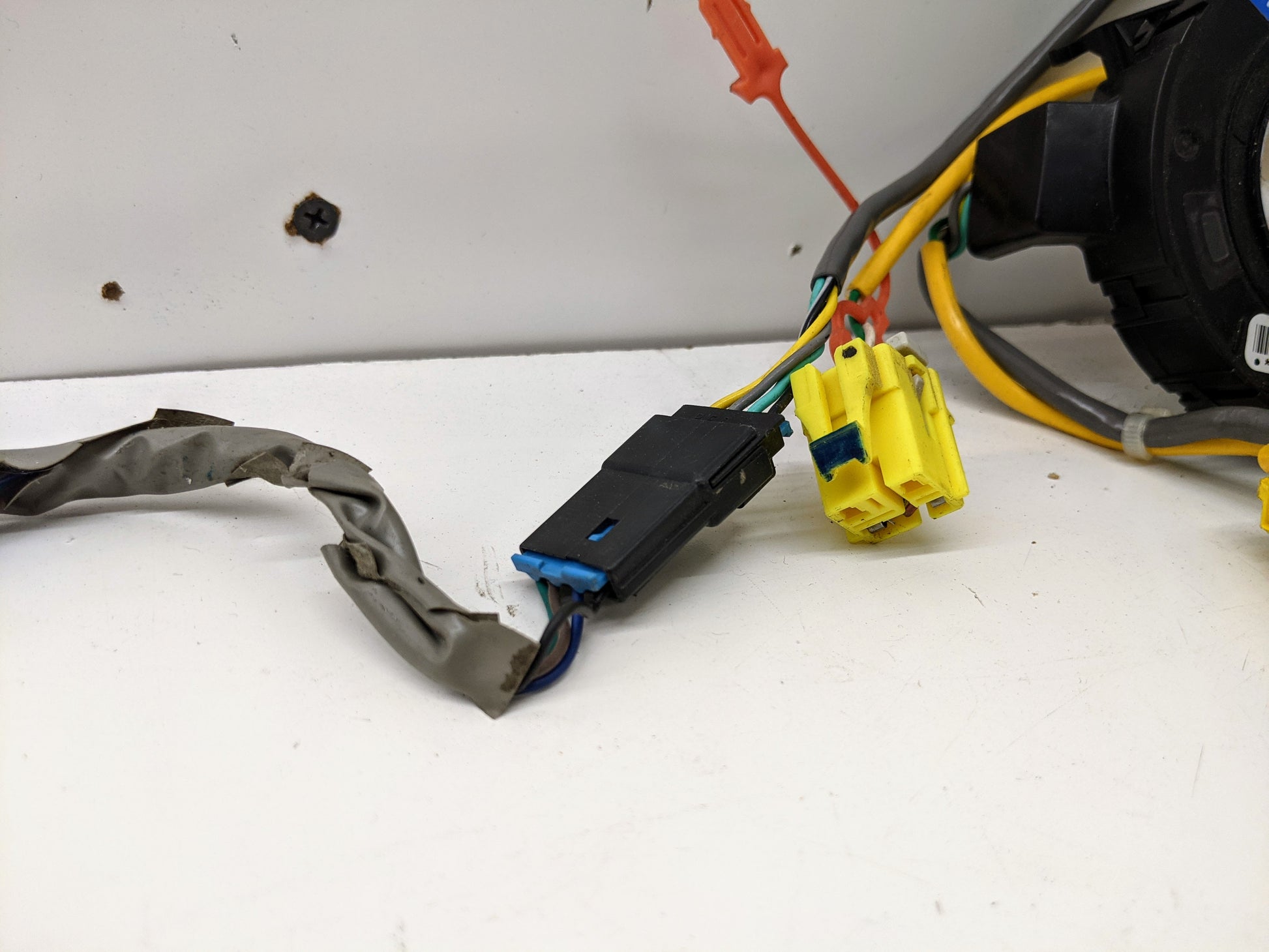 Close-up of General Motors OEM Steering Wheel SRS Air Bag Clock Spring with radio controls, tested for 2004-2005 Chevy S10 Blazer. Features black and yellow plastic plugs and wires wrapped in metallic tape, shown against a white background.