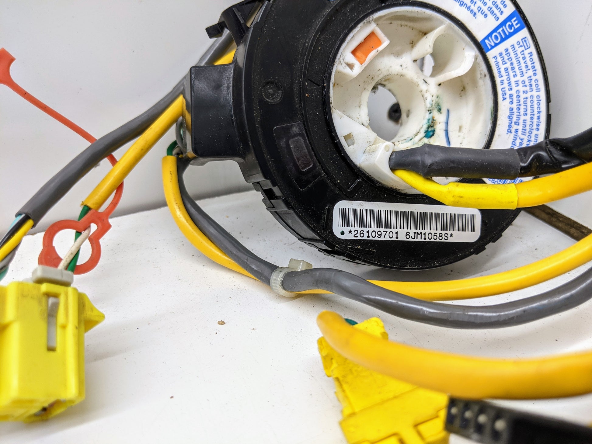 Close-up of a General Motors OEM Steering Wheel SRS Air Bag Clock Spring w/Radio Controls, tested for 2004-2005 Chevy S10 Blazer, showing yellow and gray wires, barcode label, warning stickers, and steering wheel control connectors.
