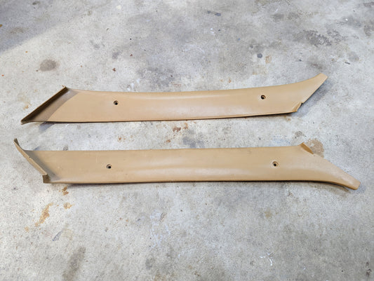 Two tan OEM General Motors A Pillar Trim Panels (64I) for 1982-1993 Chevrolet S10, Blazer, and more, shown parallel with screw holes on a concrete floor—ideal originals for restoration or upgrade.