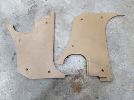 A pair of tan 64I OEM kick panel knee trim by General Motors for 1982-1993 Chevrolet S10, Blazer, and more are shown with screw holes and curved edges, lying on a concrete floor.