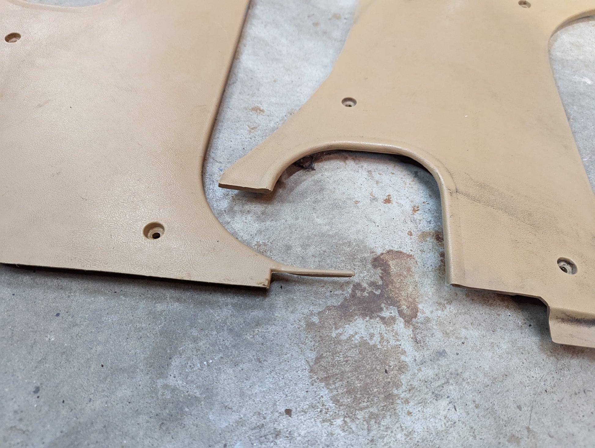 Two OEM General Motors tan 64I kick panel knee trim pieces for 1982-1993 Chevrolet S10, Blazer, and more rest on concrete; one has a broken edge, while the other retains a rounded cutout.