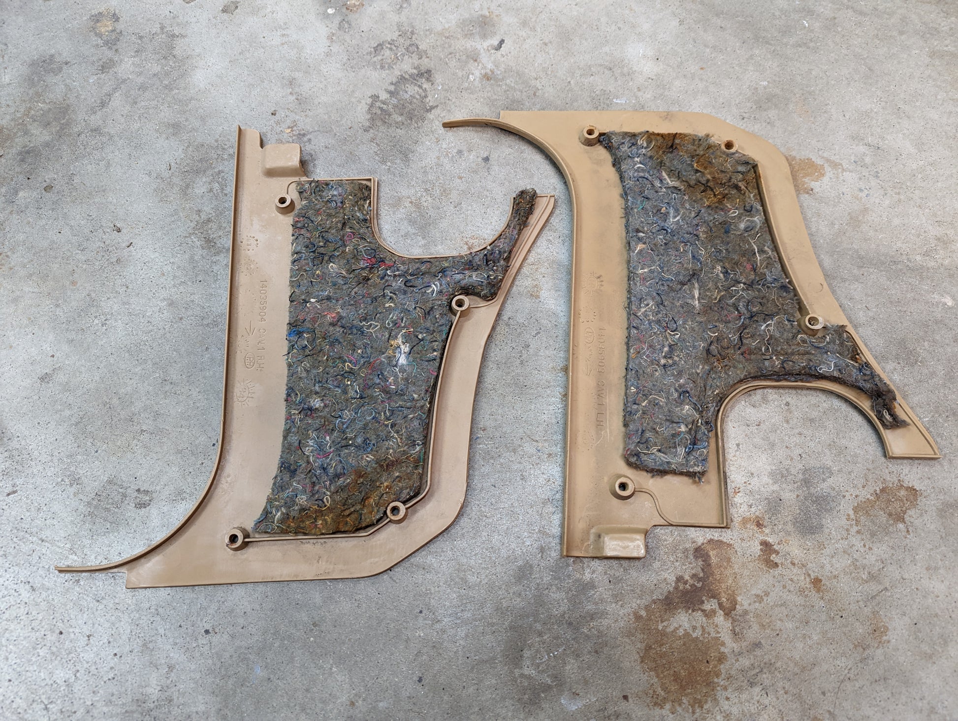 A pair of General Motors OEM tan 64I kick panel knee trim for 1982–1993 Chevrolet S10, Blazer, and more are lying side by side on a concrete floor, showing visible screws and stains on the panels and floor.