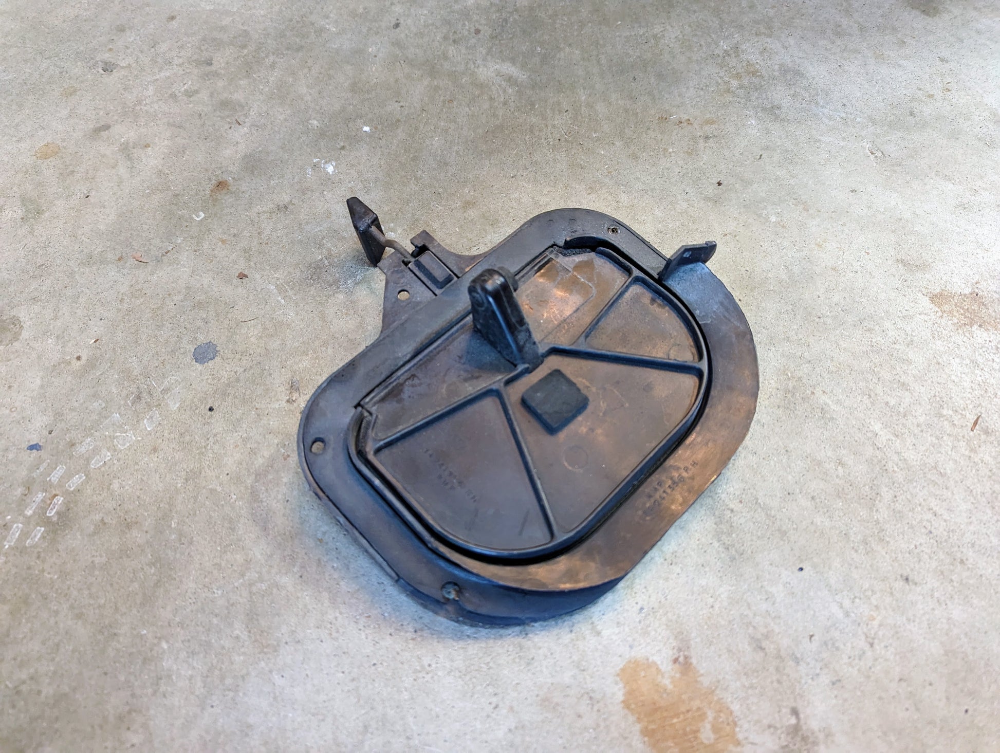 A black plastic OEM Fresh Air Floor Vent Door by General Motors for 1982-1993 Chevrolet S10 and Blazer rests on a concrete surface, detached and showing dirt and scratches typical of used vent doors.