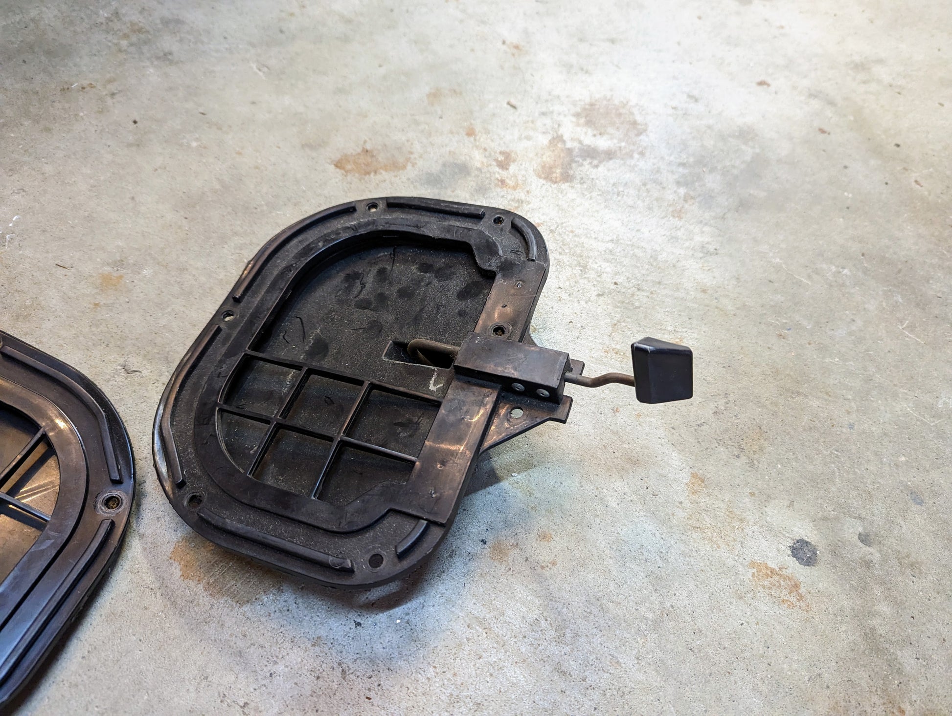 A General Motors OEM Fresh Air Floor Vent Door for 1982-1993 Chevrolet S10/Blazer lies on concrete, displaying its latch and interior. This black plastic door resembles OEM vent and 1982-85 kick panel doors.