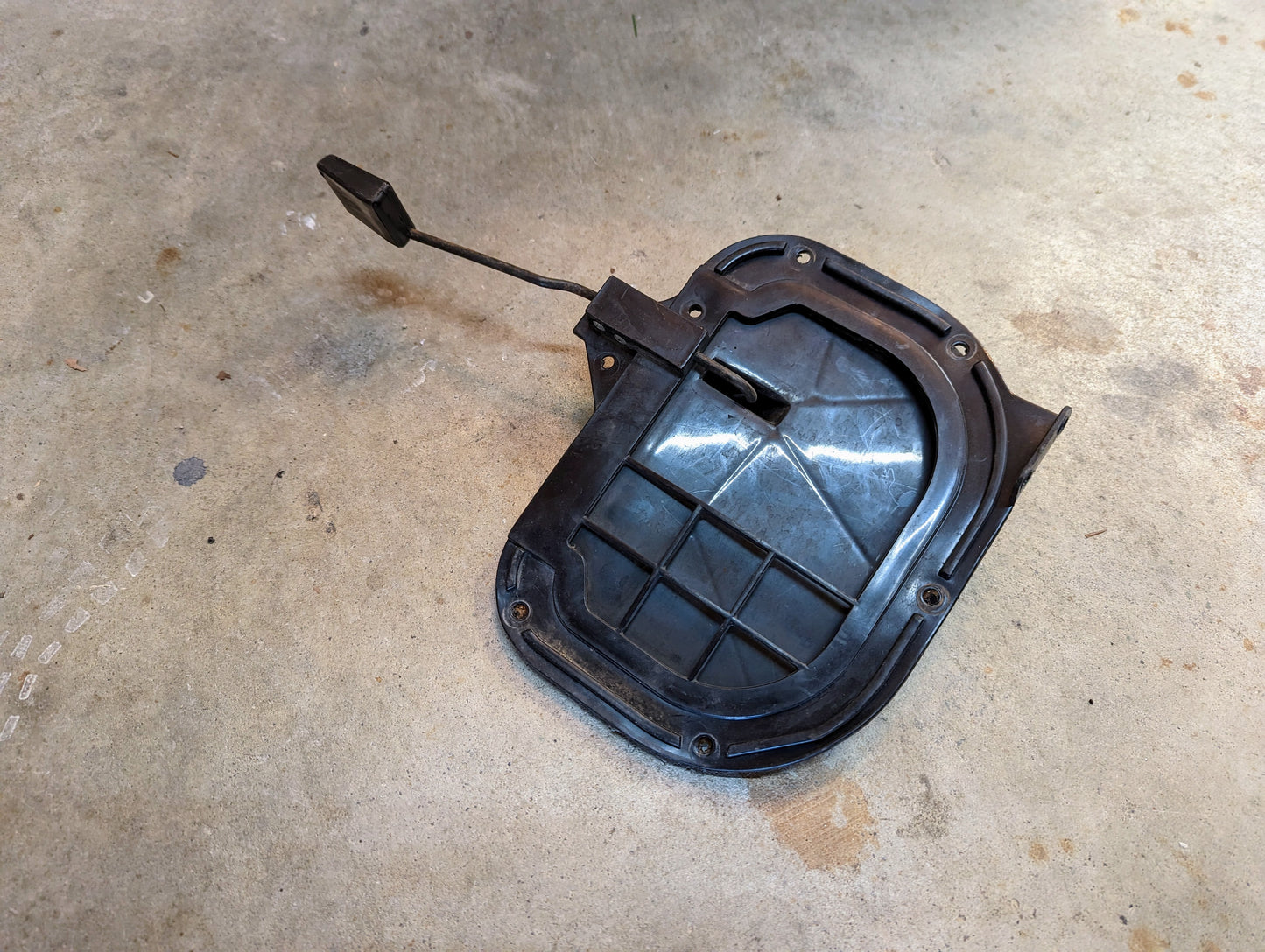 A General Motors OEM Fresh Air Floor Vent Door Driver-Side LH for 1982-1993 Chevrolet S10, Blazer, and more is shown; its a black plastic automotive part with an attached hinge and spring on a concrete floor.