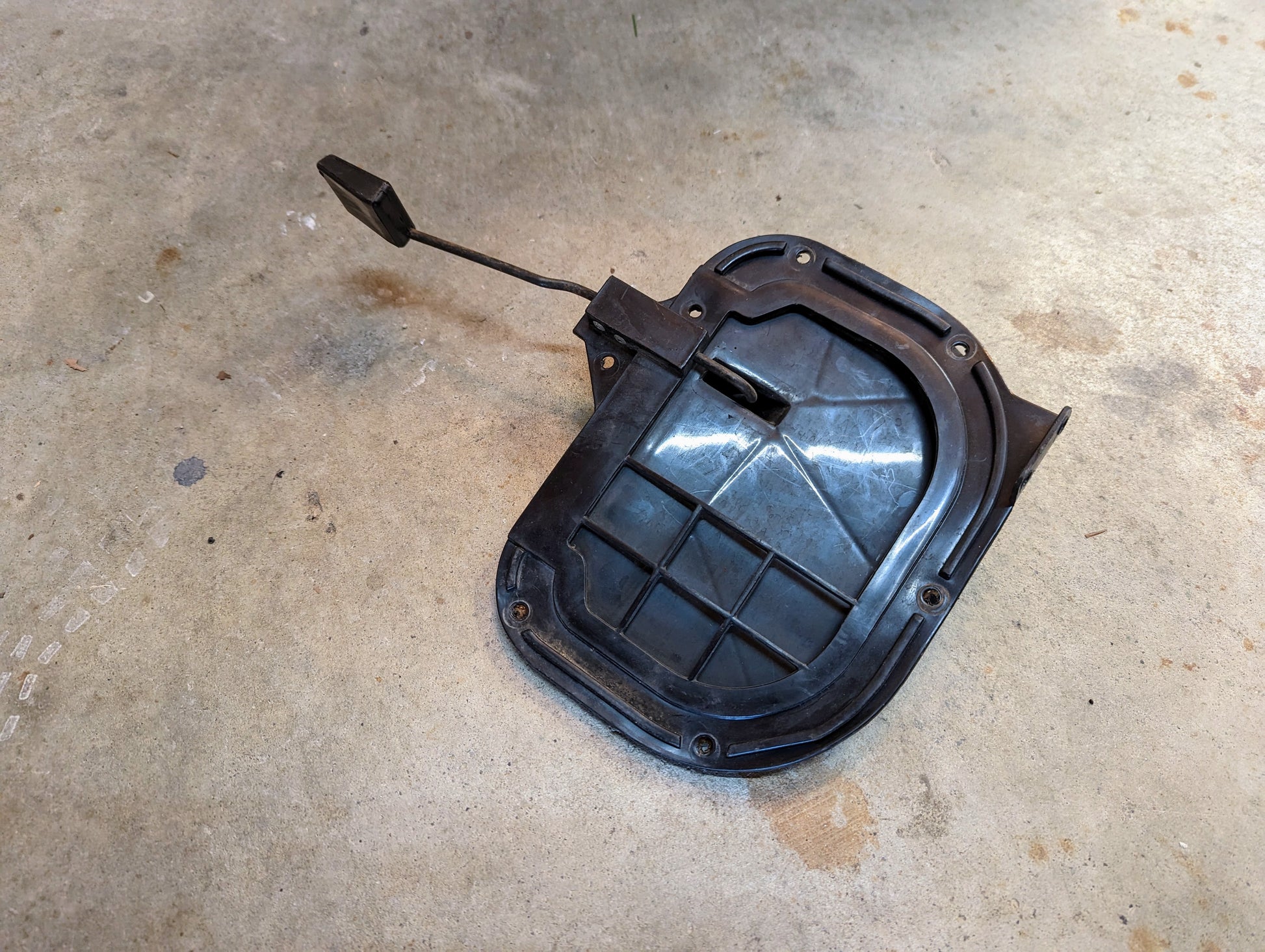 A General Motors OEM Fresh Air Floor Vent Door Driver-Side LH for 1982-1993 Chevrolet S10, Blazer, and more is shown; its a black plastic automotive part with an attached hinge and spring on a concrete floor.