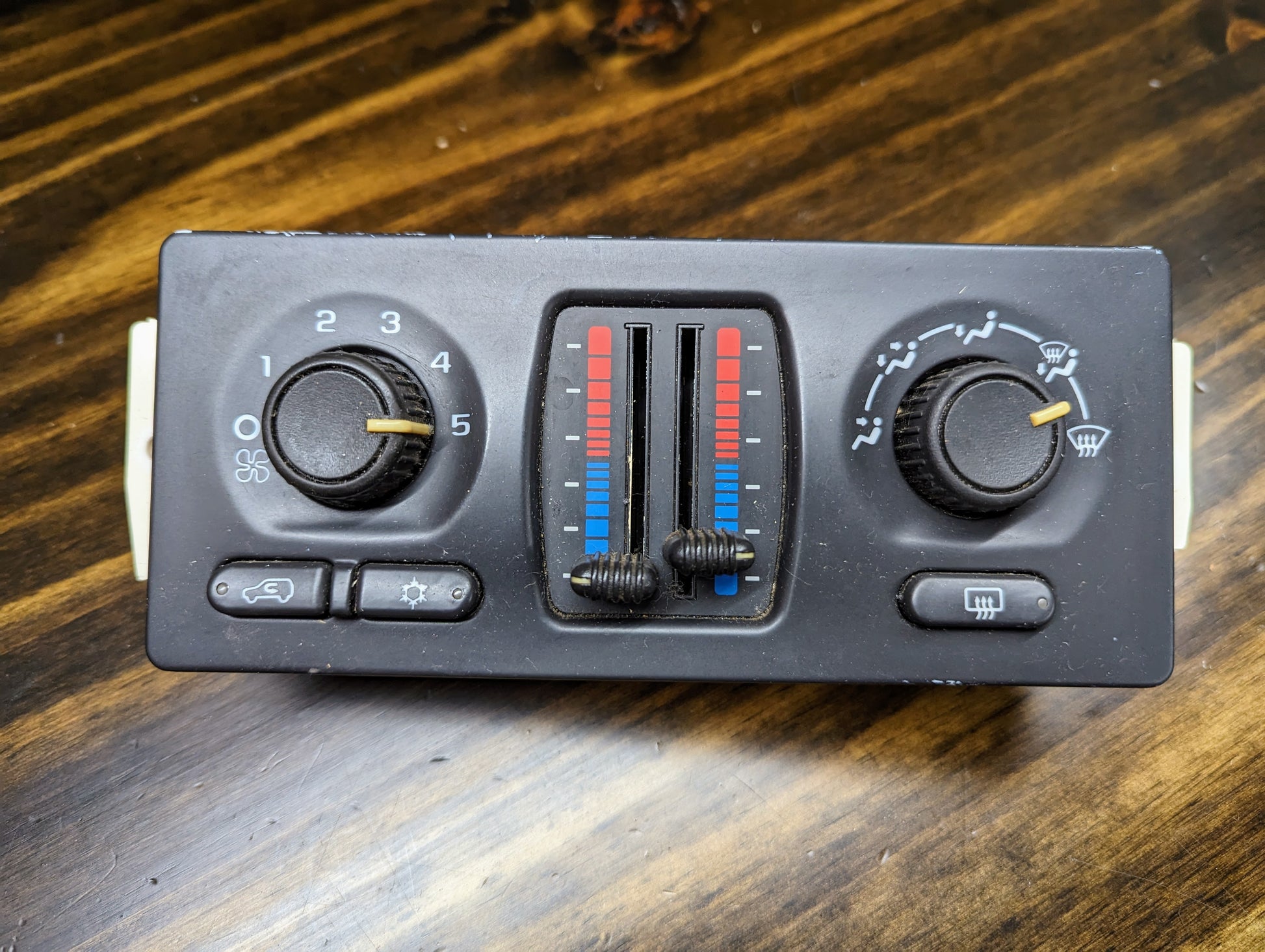 The General Motors OEM Dual Climate HVAC Manual Control Head w/Rear Defrost for 2003-2006 GM Full Size Trucks features fan speed dials, red/blue temperature sliders, and buttons for recirculation, rear defrost, and airflow direction.