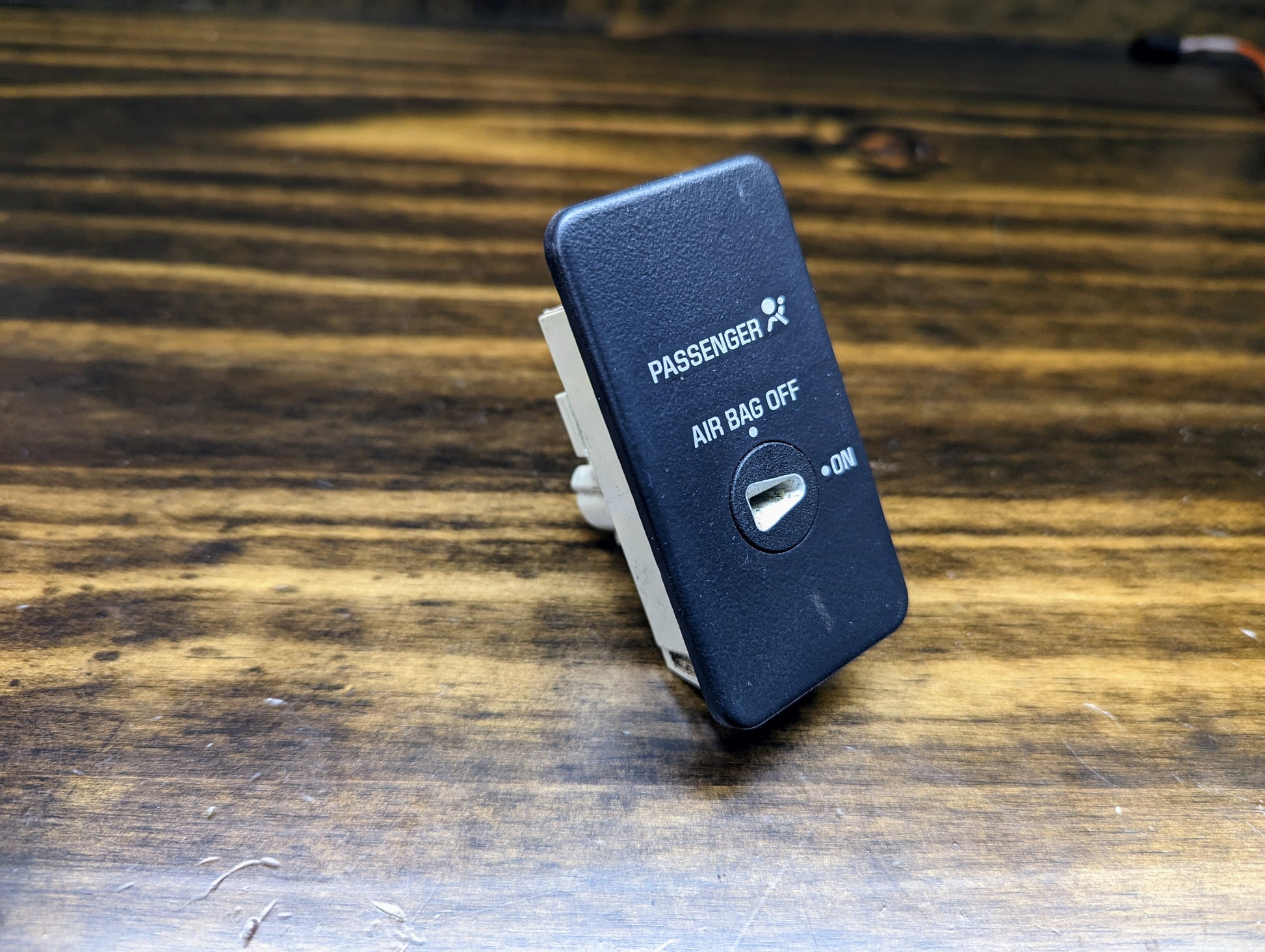 A General Motors OEM Passenger Inflatable Restraint Air Bag Key Switch for 1998-2003 Chevy S10 & GMC Sonoma with AIR BAG OFF/ON labels and key slot is shown resting on a wooden surface.