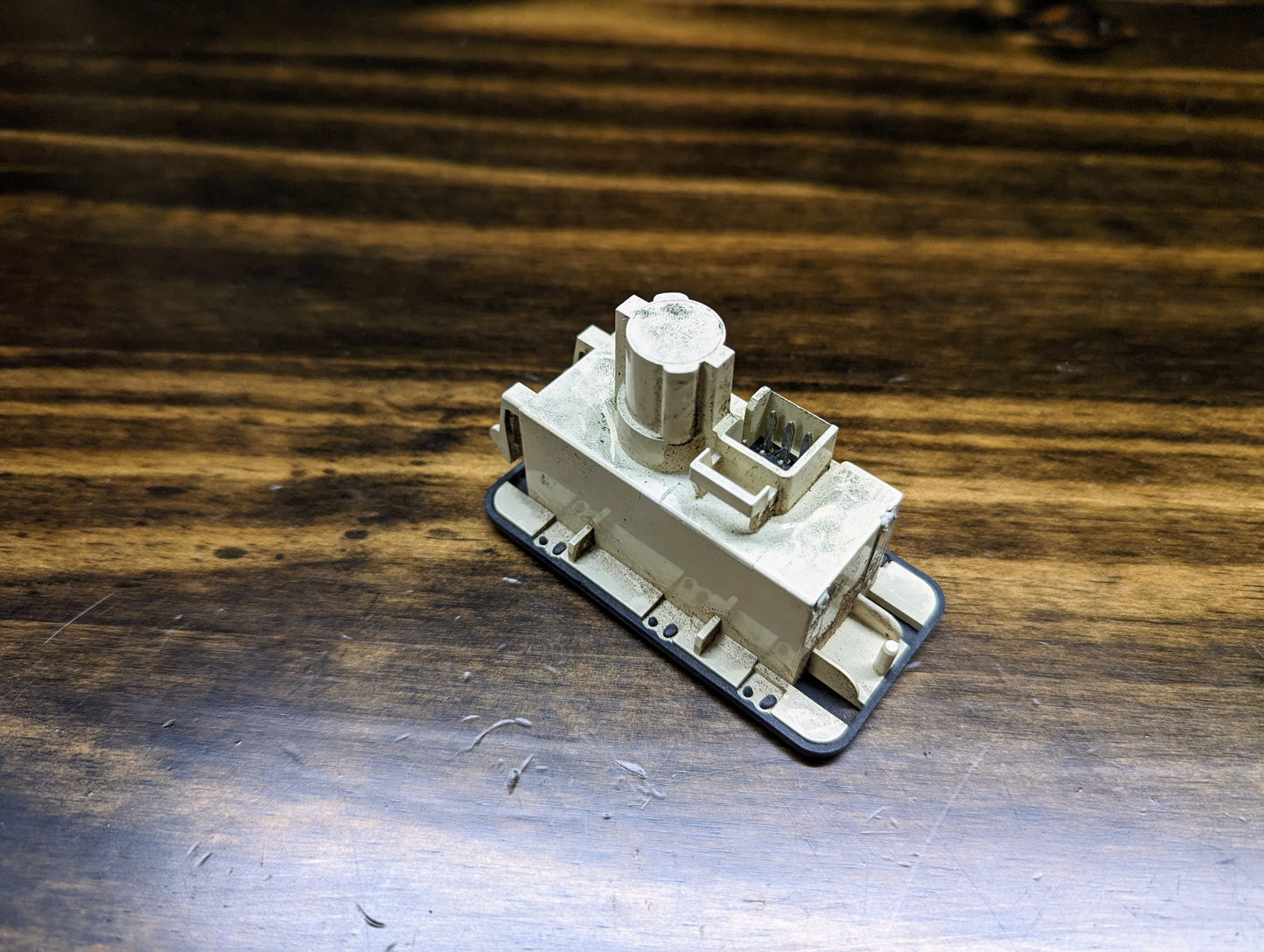 A small, beige plastic locomotive model rests on a wooden surface beside a slightly worn General Motors OEM Passenger Inflatable Restraint Air Bag Key Switch for 1998-2003 Chevy S10 & GMC Sonoma, adding automotive character to the scene.