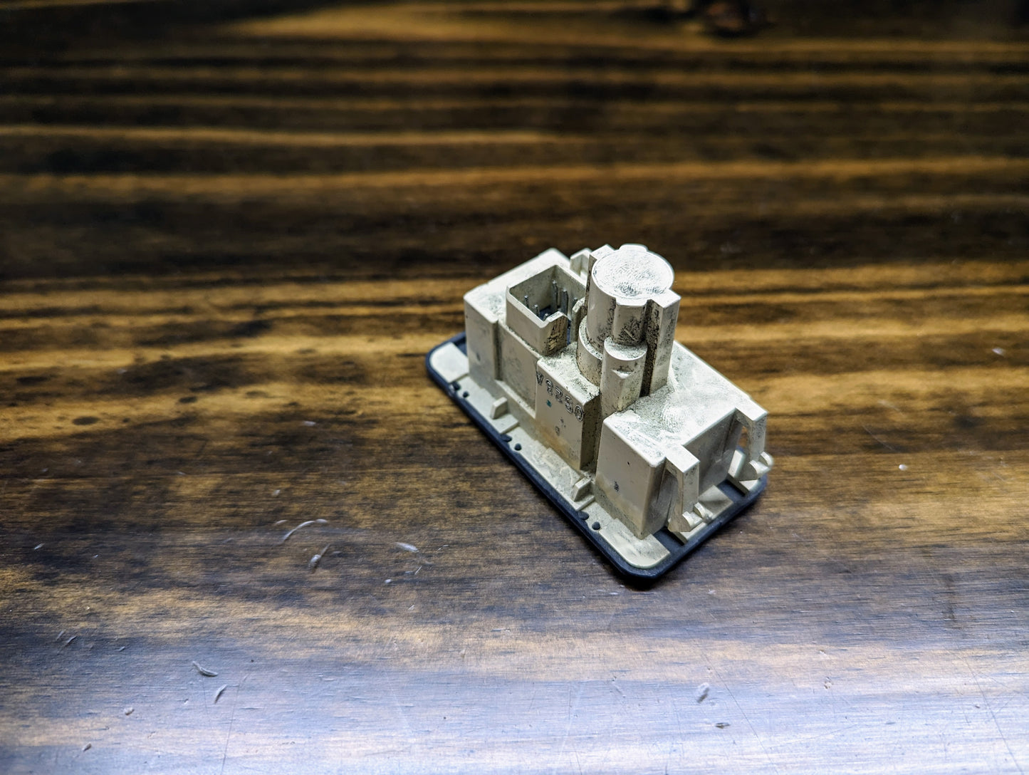 A small beige rectangular 3D-printed model sits on a dark wooden surface, featuring geometric shapes and levels inspired by the OEM Passenger Inflatable Restraint Air Bag Key Switch for 1998-2003 Chevy S10 & GMC Sonoma by General Motors.