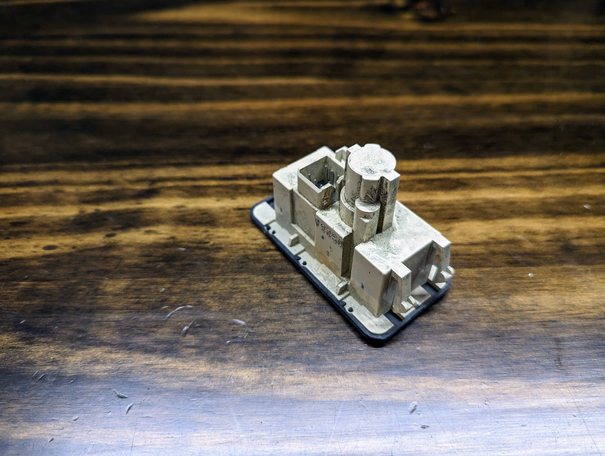 A small beige rectangular 3D-printed model sits on a dark wooden surface, featuring geometric shapes and levels inspired by the OEM Passenger Inflatable Restraint Air Bag Key Switch for 1998-2003 Chevy S10 & GMC Sonoma by General Motors.