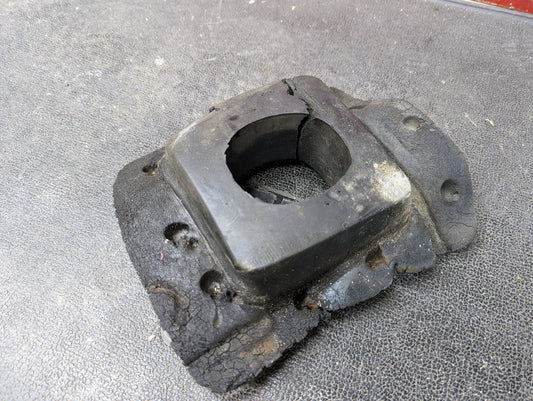 A worn Manual Floor Shifter Insulator Foam from General Motors for 1998-2005 Chevy S10, Blazer, GMC Sonoma, or Jimmy sits on a textured black surface, showing signs of age and deterioration.