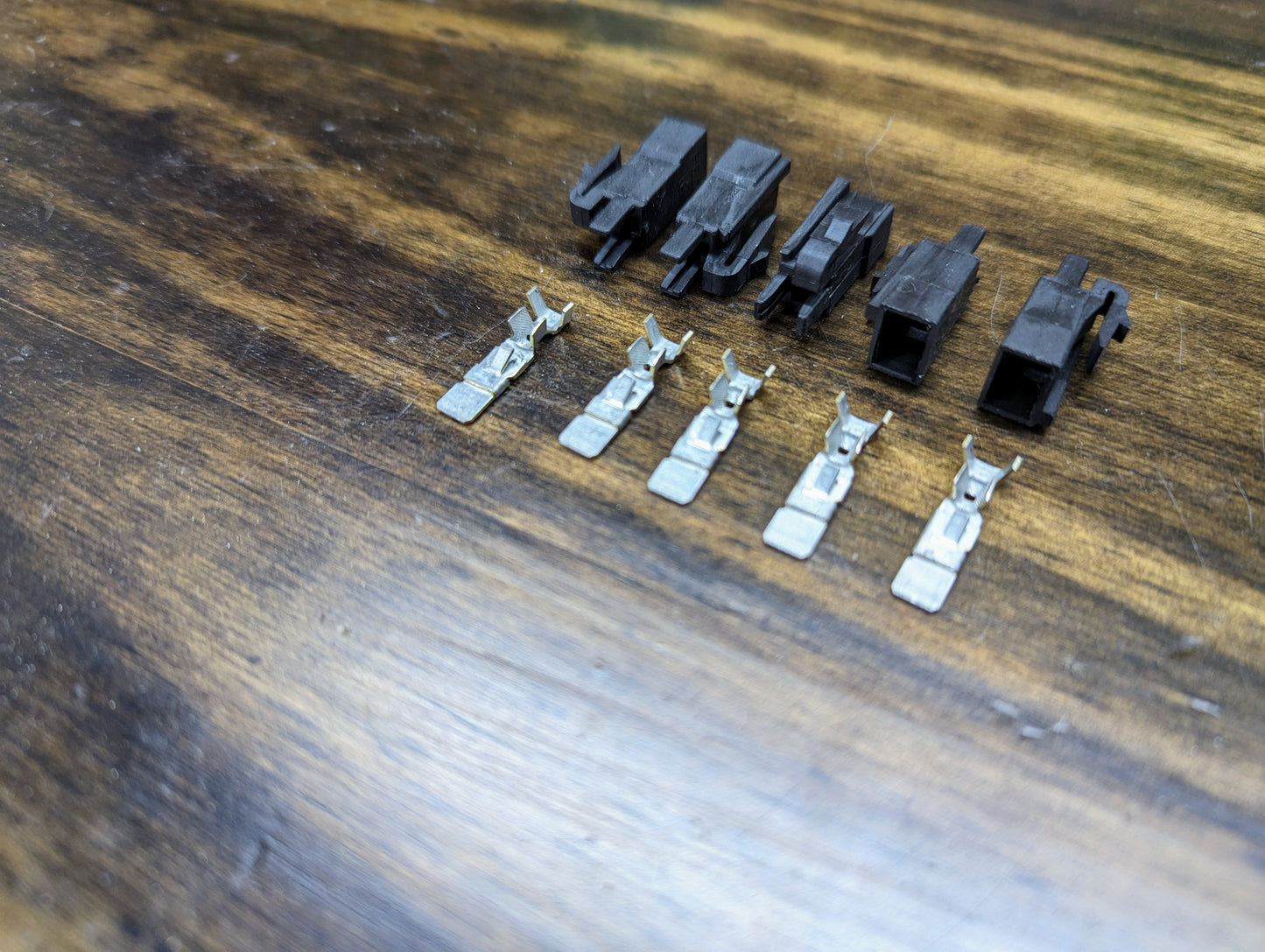 Five Aptiv KIT Power Tap Connectors and five terminals for under dash fuse panels, compatible with many 80s & 90s vehicles, are arranged in two rows on wood: connectors at the back, terminals in front.