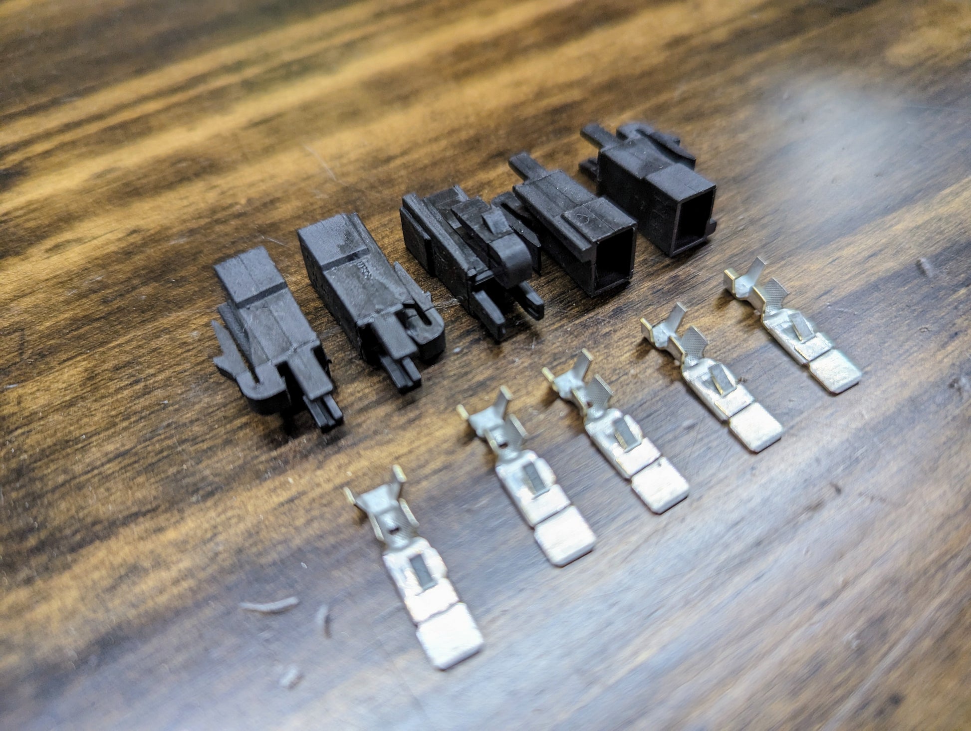 Six Aptiv KIT Power Tap Connector housings and six terminals for under dash fuse panels, designed for many 80s & 90s vehicles, are arranged on a wooden surface with the housings at the back and terminals in front.