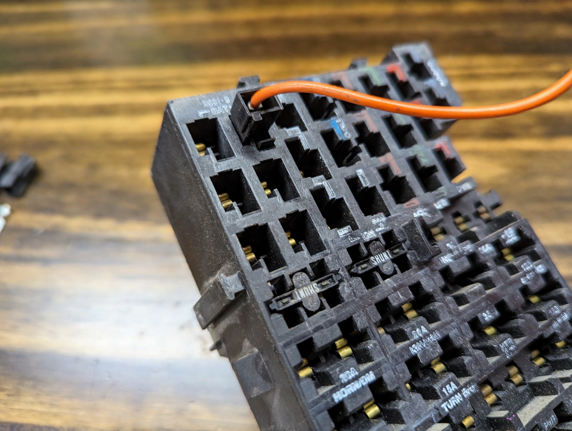Close-up of an Aptiv KIT Power Tap Connector & Terminals for under dash fuse panels in many 80s & 90s vehicles, showing multiple empty slots and a red wire inserted, using GM truck terminals on a wooden surface.