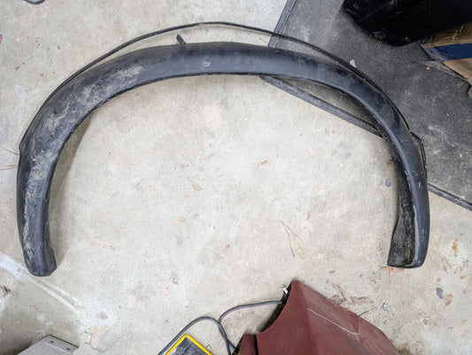 A General Motors OEM passenger rear bed flare extension for a 1994-2004 Chevy S10 or GMC Sonoma rests on a dirty, scratched concrete surface, with parts of a red object and an item with yellow edges nearby.