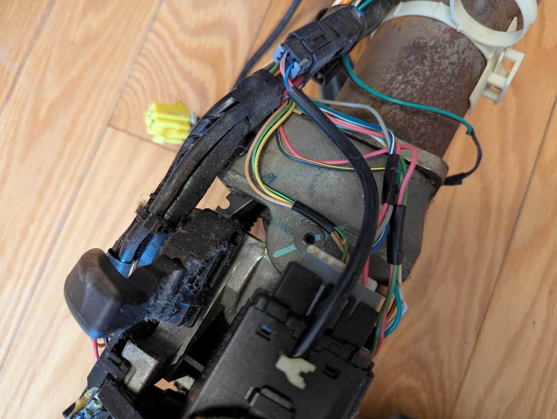 A close-up view of a General Motors OEM Steering Column for 2003-2006 GM Full Size Trucks, showing various colored wires, connectors, and mechanical parts against a wooden floor background.