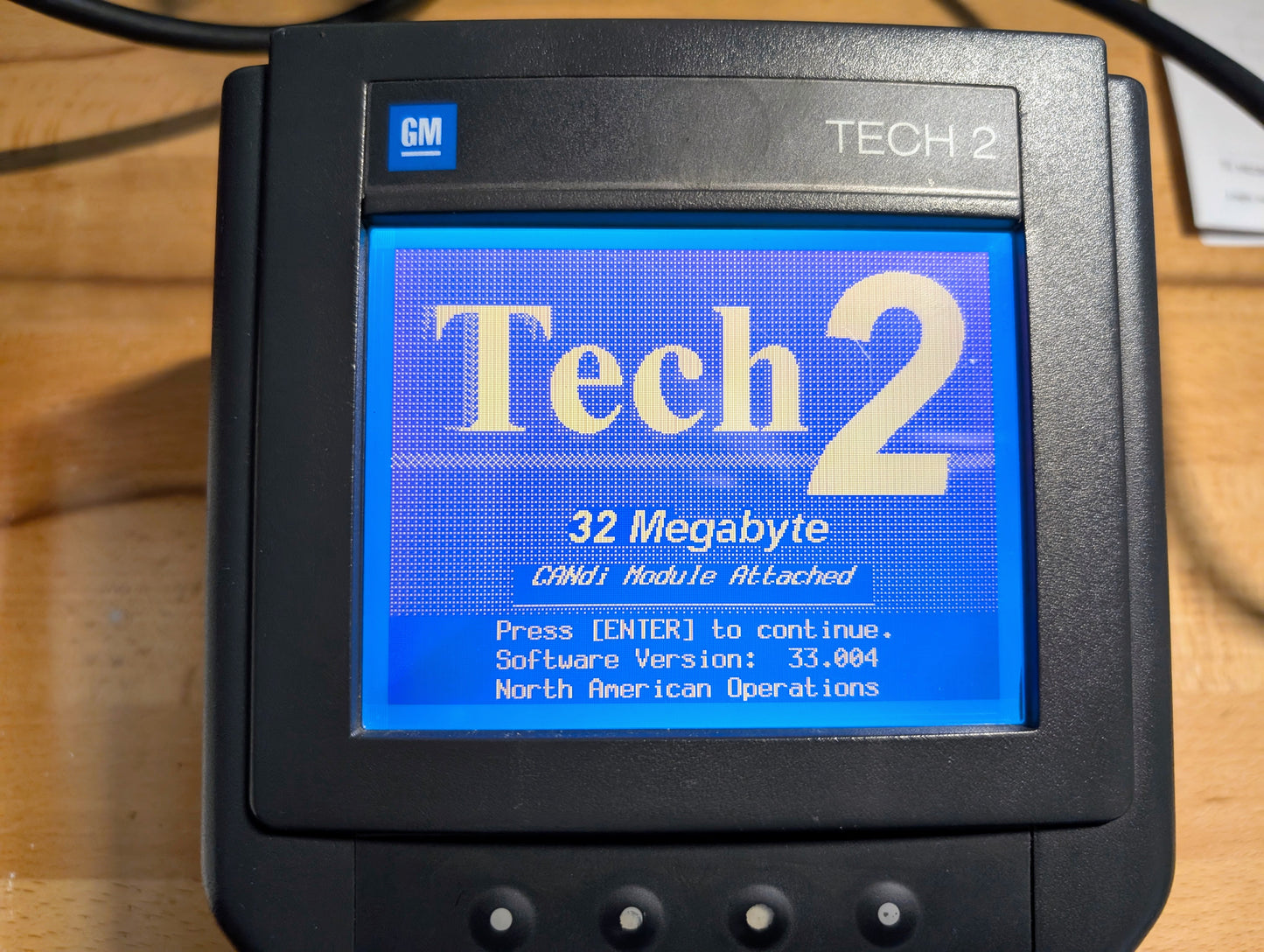 A close-up of the Vetronix TESTED Tech 2 Automotive Diagnostic Tool & Accessories for 1991-2013 GM Vehicles shows “Tech 2, 32 Megabyte, CANDI Module Attached,” instructions, and software version 33.004 on its blue screen.