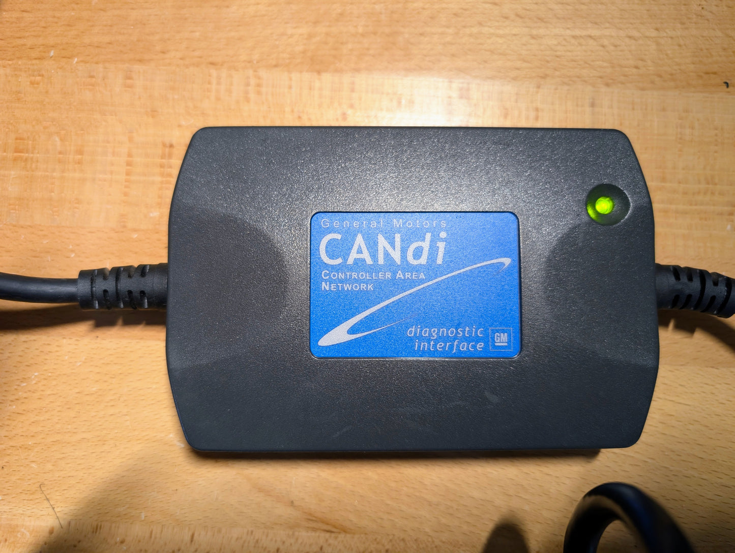 A Vetronix TESTED Tech 2 Automotive Diagnostic Tool & Accessories for 1991-2013 GM Vehicles, featuring a green indicator light, rests on a wooden surface; its label shows Controller Area Network and diagnostic interface.