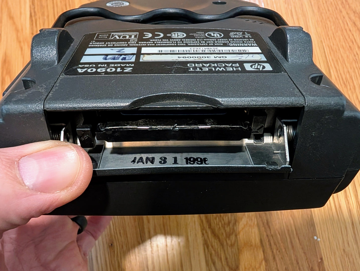 A close-up of a hand holding an HP battery pack with its compartment open, showing metal contacts and numbers—demonstrating the precision seen in the Vetronix TESTED Tech 2 Automotive Diagnostic Tool & Accessories for GM vehicles.