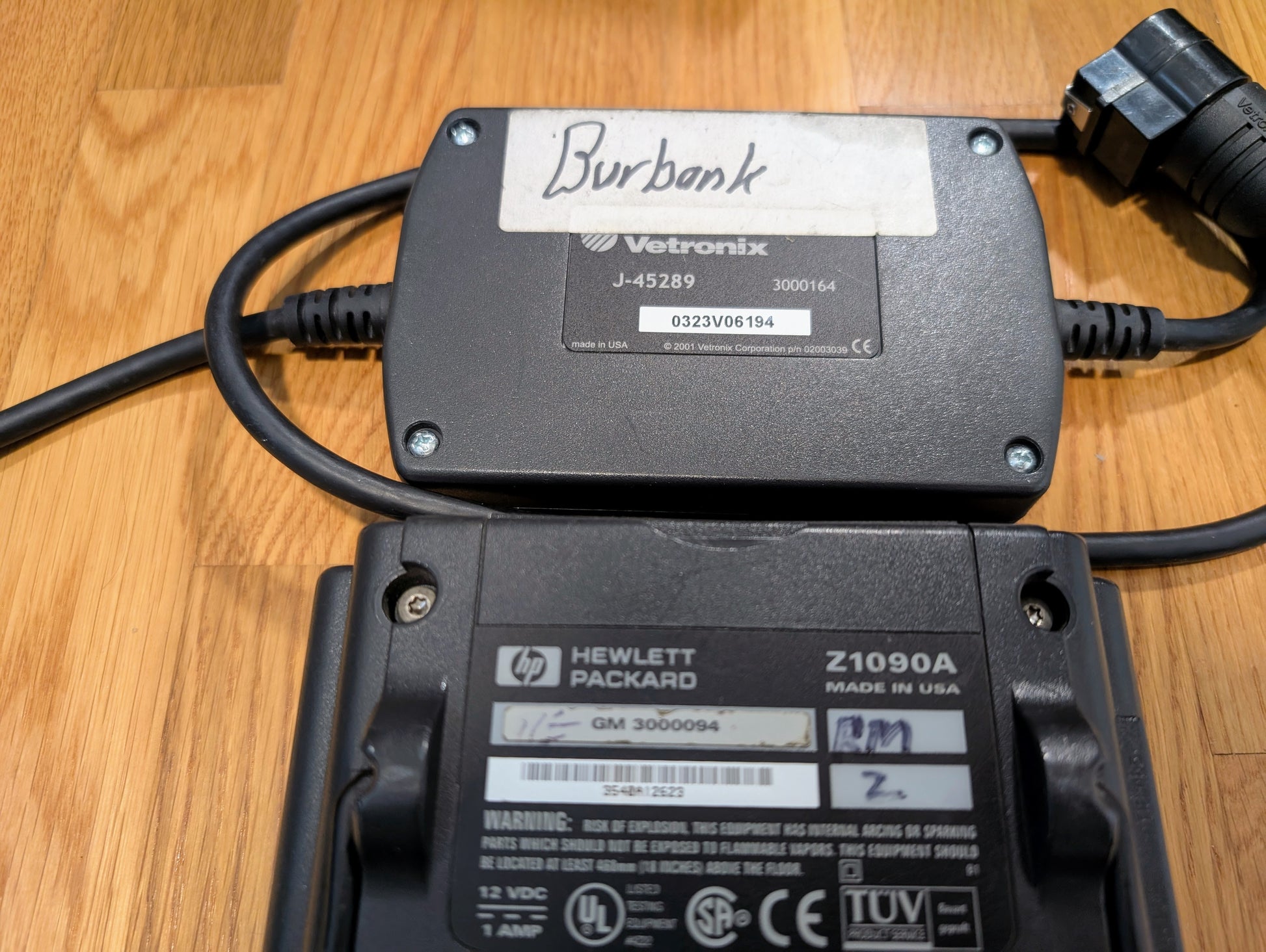 A Vetronix TESTED Tech 2 Automotive Diagnostic Tool & Accessories for 1991-2013 GM vehicles is connected to a Hewlett Packard Z1090A component, both resting on a wooden surface with visible cords and labels.