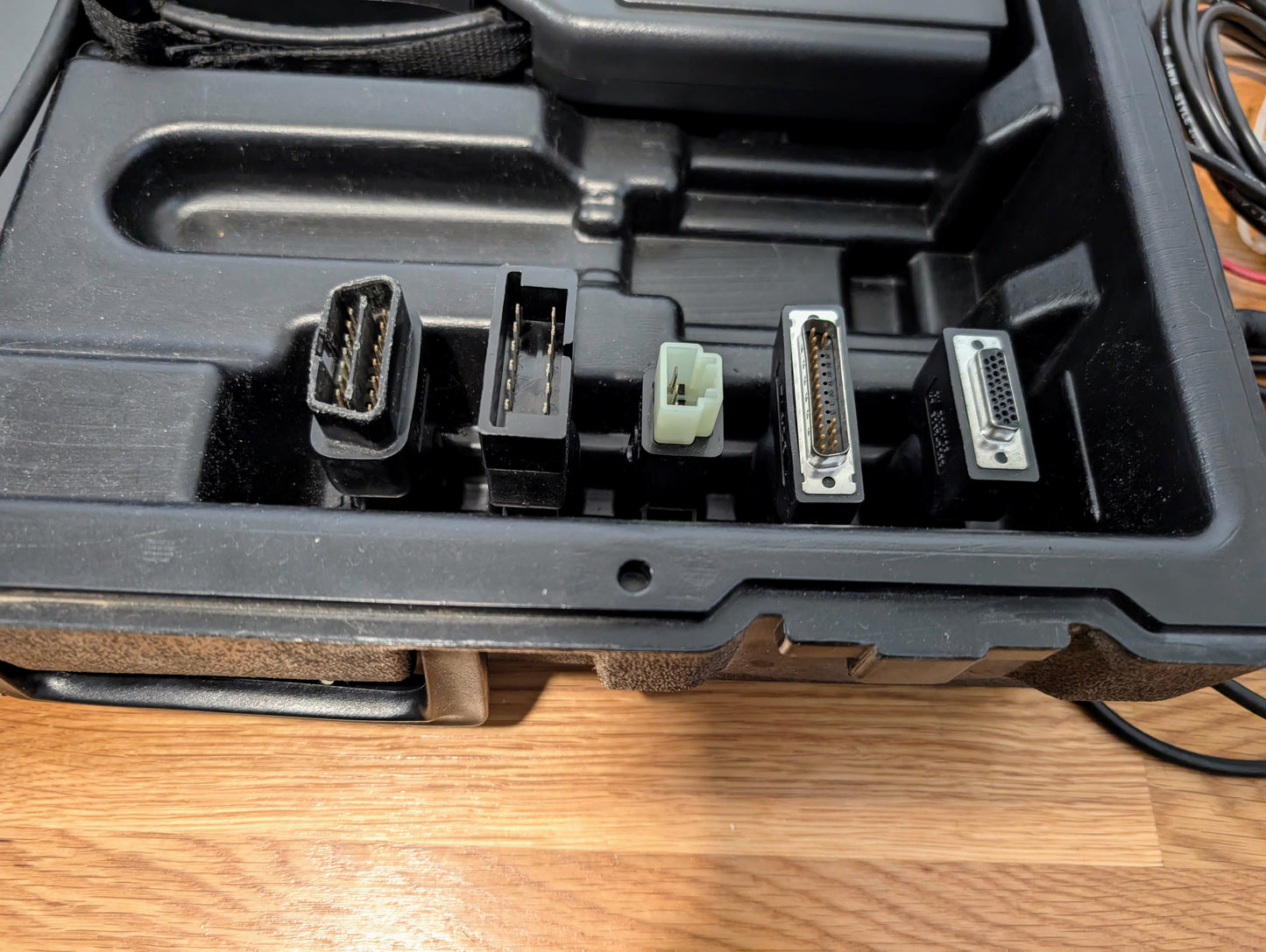 A close-up of a black plastic case holding five connectors, arranged in a row on wood—perfect for use with the Vetronix TESTED Tech 2 Automotive Diagnostic Tool & Accessories for 1991–2013 GM vehicles.