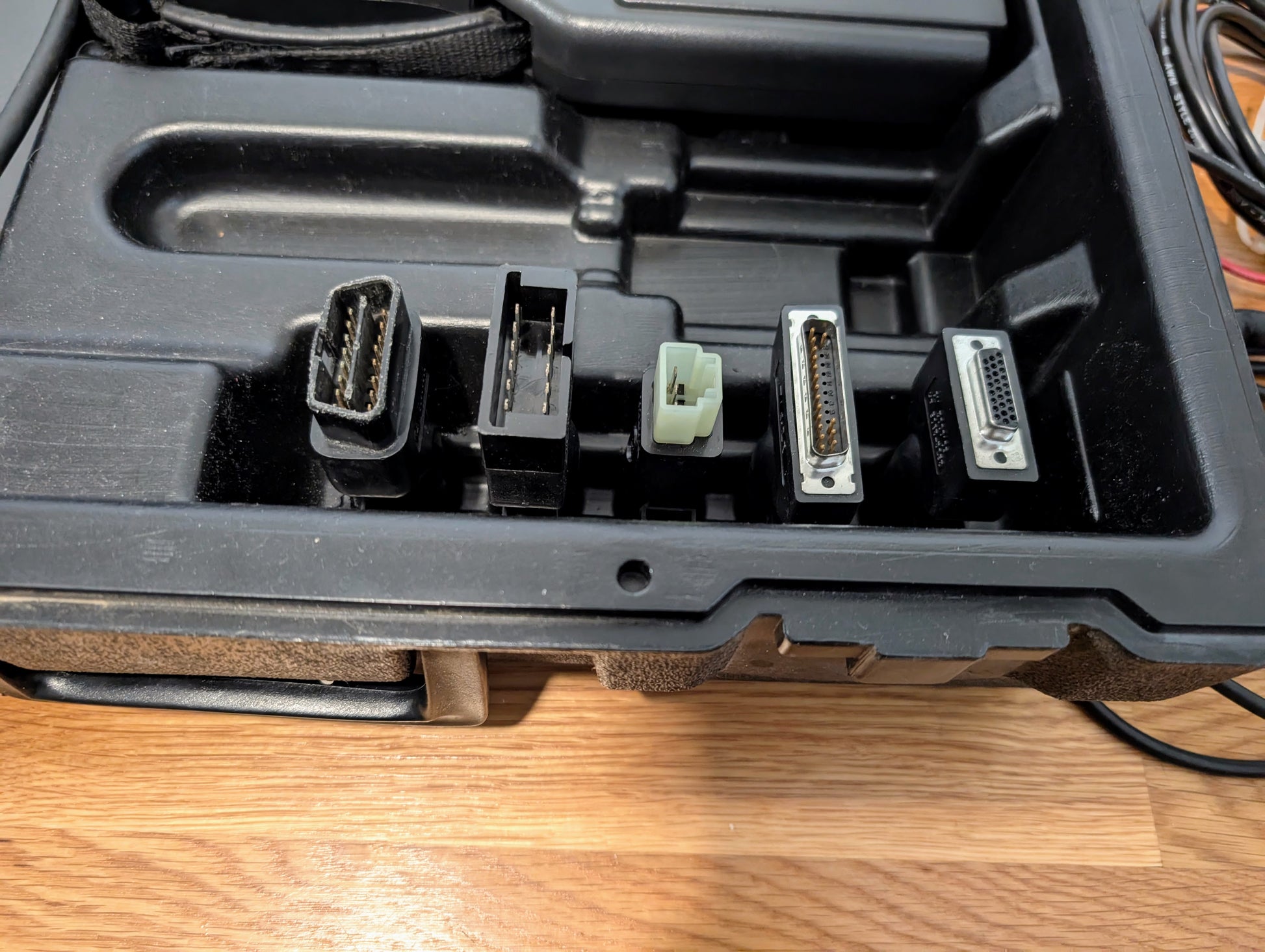 A close-up of a black plastic case holding five connectors, arranged in a row on wood—perfect for use with the Vetronix TESTED Tech 2 Automotive Diagnostic Tool & Accessories for 1991–2013 GM vehicles.