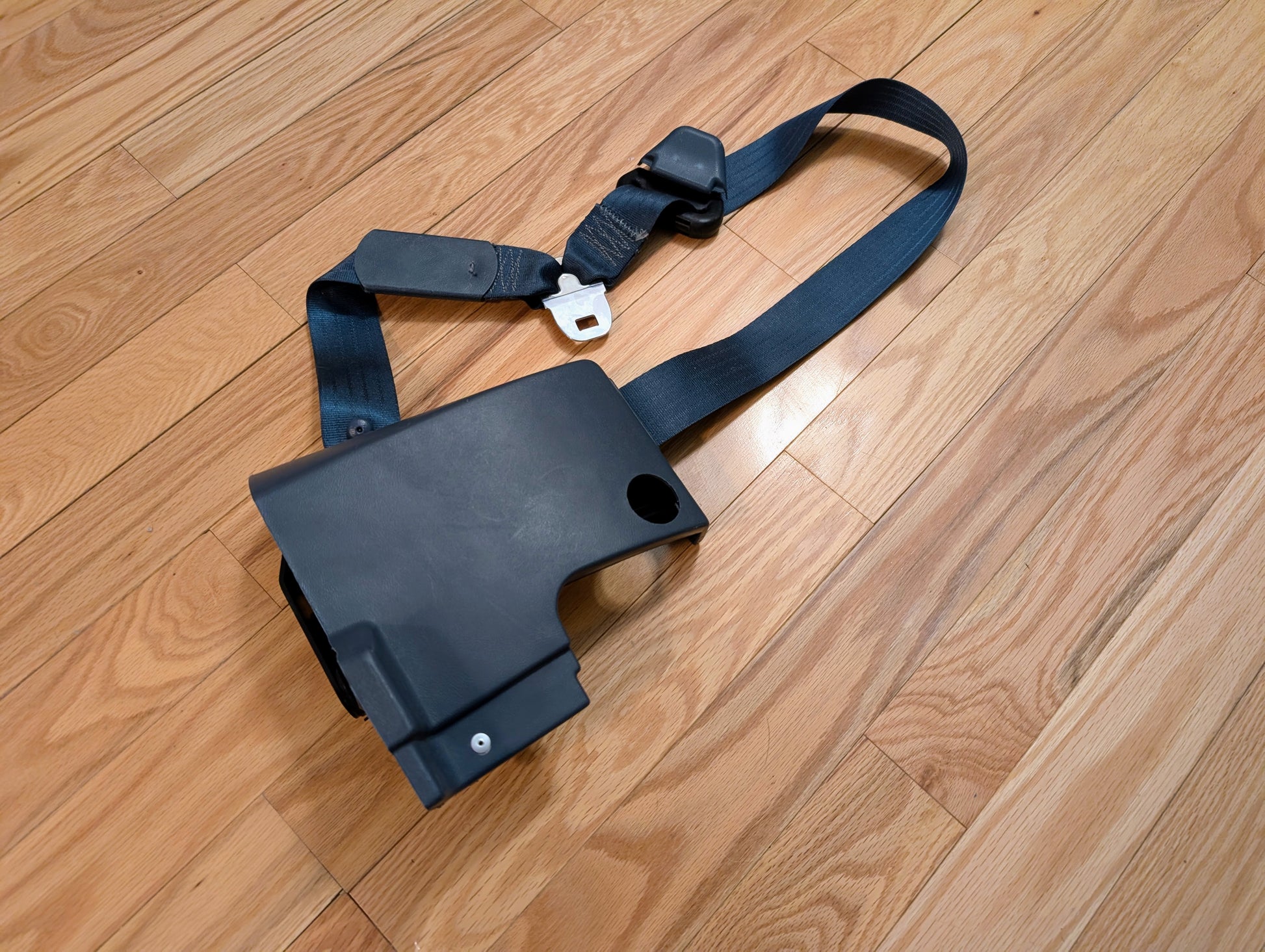 A blue General Motors NOS passenger seat belt retractor for 1982–1993 Chevy S10 or GMC S15 rests on a light wood floor—ideal for extended cab seat belt replacement or upgrade.