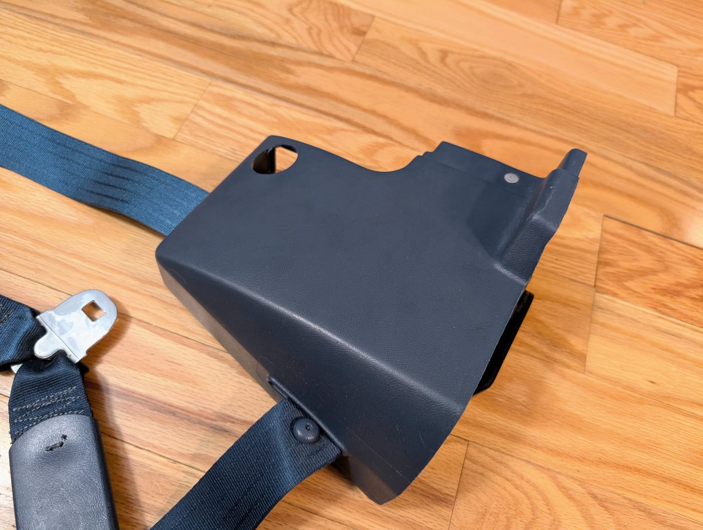 A General Motors NOS blue passenger seat belt retractor for 1982-1993 Chevy S10 or GMC S15 is shown on a light brown wooden floor.