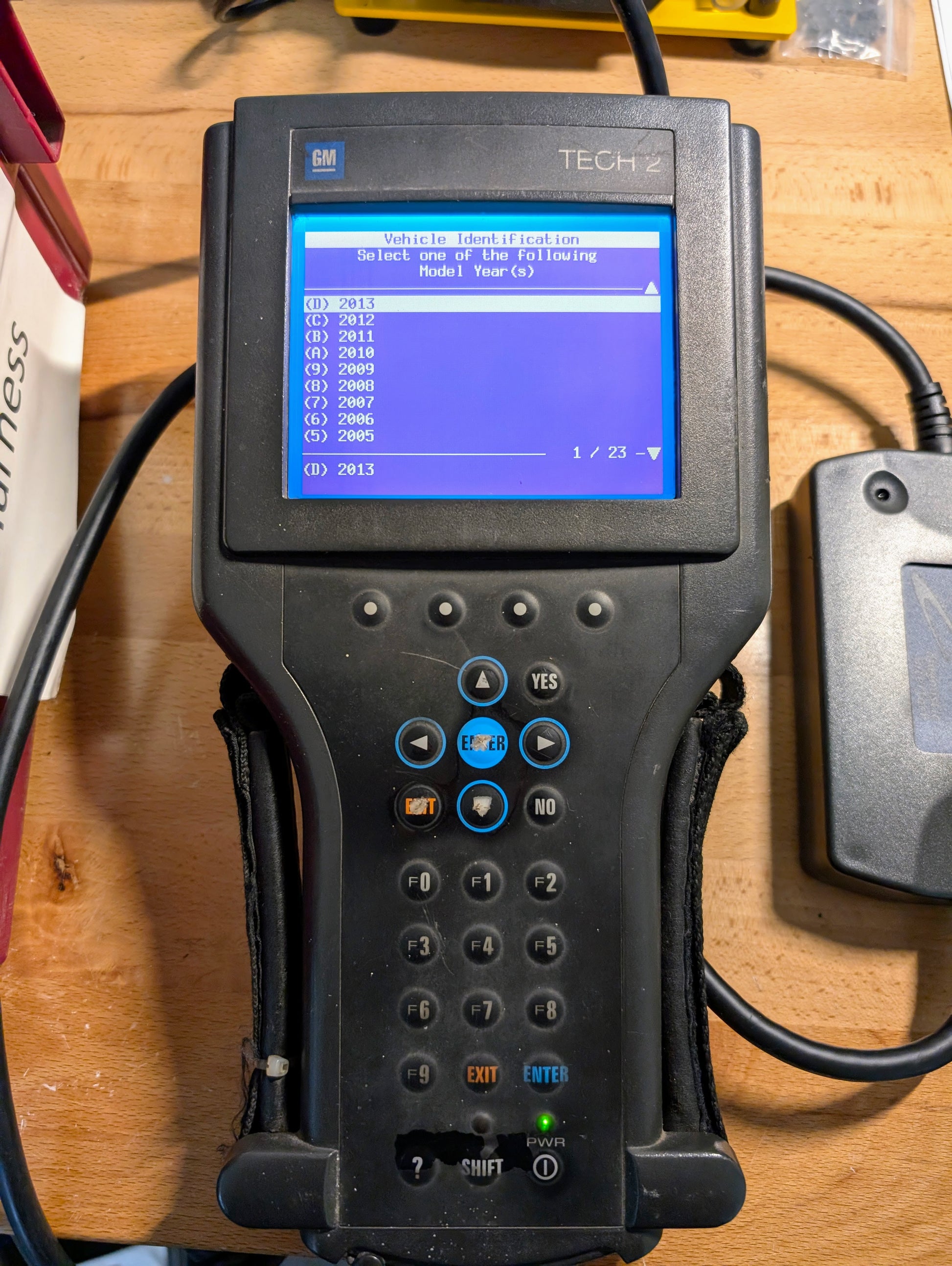 A Vetronix TESTED Tech 2 Automotive Diagnostic Tool & Accessories for 1991-2013 GM vehicles is shown on a wooden workbench, displaying its blue screen often used by dealer technicians.