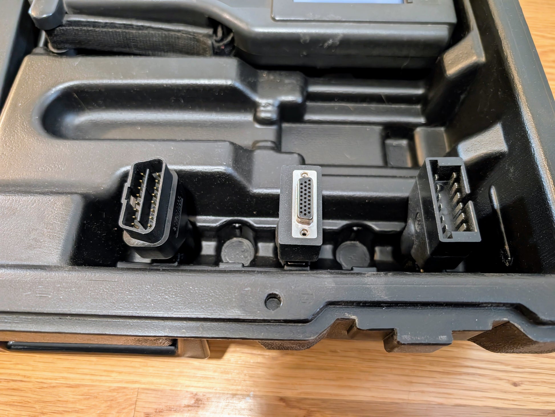 Three Vetronix TESTED Tech 2 Automotive Diagnostic Tool connectors for 1991-2013 GM vehicles are displayed in a black, slotted plastic case. Each connector features a distinct shape and pin configuration, visible from above on a wooden surface.