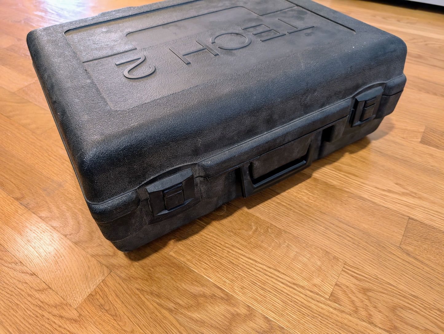 A black, hard plastic Vetronix carrying case with latches and a handle sits on a wood floor. Embossed “TECH” on the lid, it contains a TESTED Tech 2 Automotive Diagnostic Tool & Accessories for 1991-2013 GM vehicles.