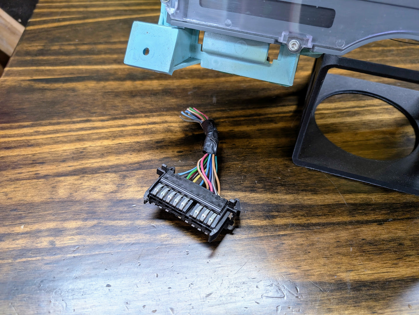A multi-colored wire harness with a black connector sits near a blue part and a bracket, likely for the General Motors OEM Instrument Cluster with PRNDL and 110 mph Speedo (1986-1994 Chevy S10 Blazer and more).
