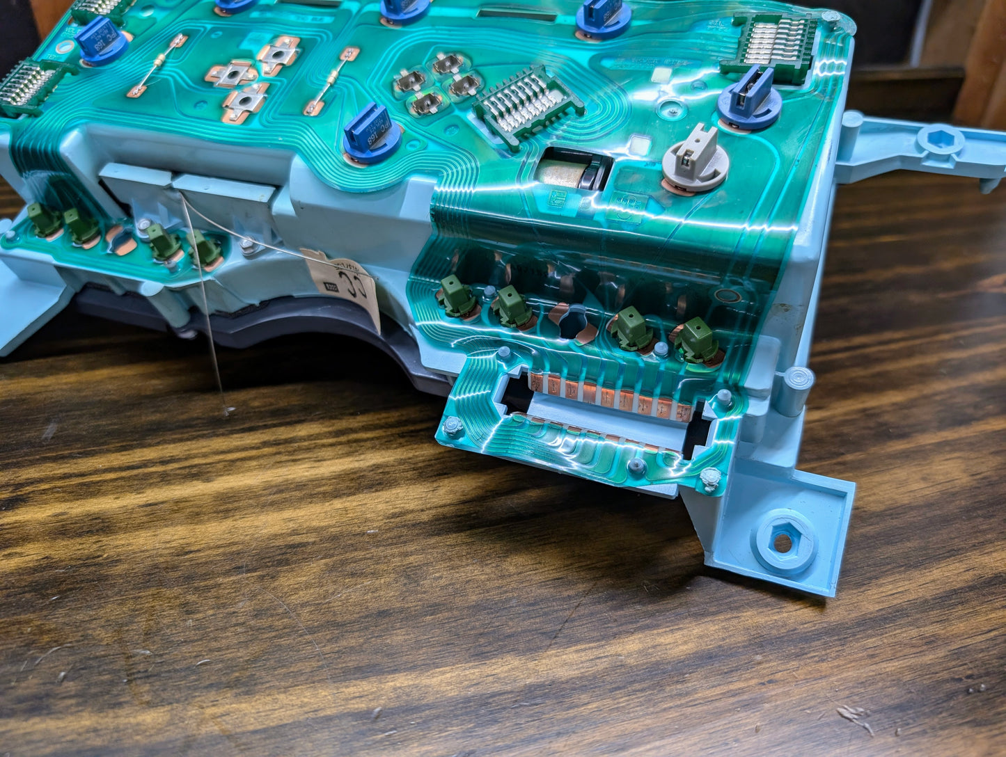 Close-up of a General Motors OEM Instrument Cluster circuit board with green traces, blue connectors, and electronic components for 1986-1994 Chevy S10 Blazer, featuring PRNDL and 110 mph speedo, on a wooden surface.