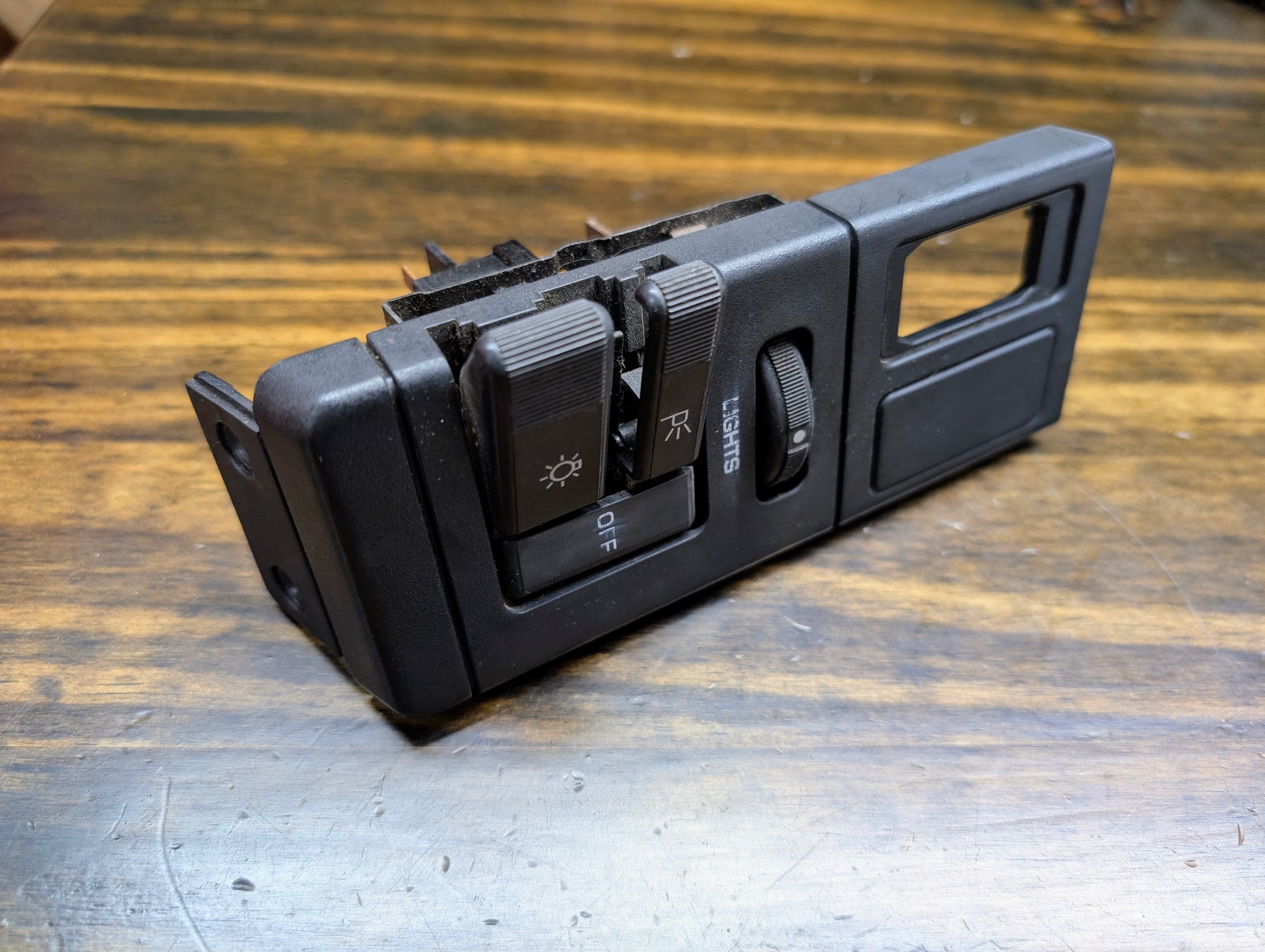 Close-up of a General Motors OEM Headlight Headlamp Switch in black for 1986-1994 Chevy S10, Blazer, GMC S15, and Jimmy on a wooden surface.