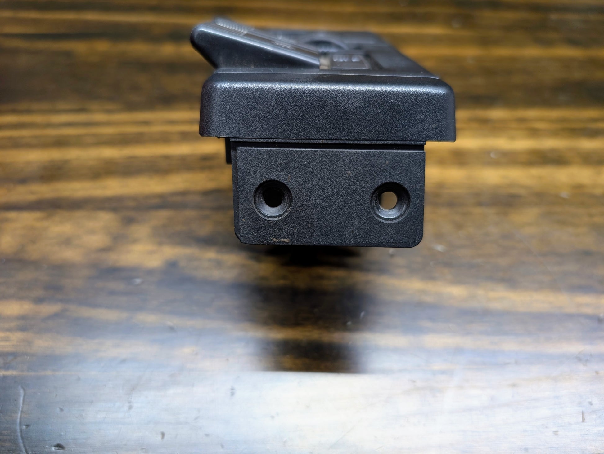 Close-up of a black OEM General Motors headlight headlamp switch for 1986-1994 Chevy S10, Blazer, GMC S15, and Jimmy. The switch features two circular holes, a textured surface, and a top latch, shown resting on wood grain.