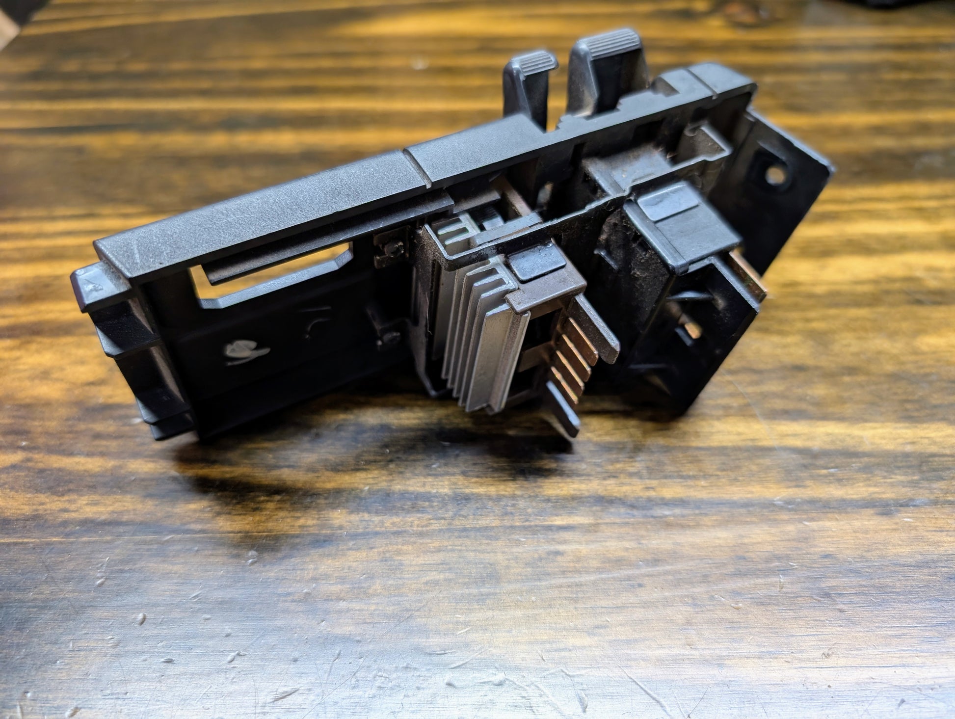 A black General Motors OEM headlight switch for 1986-1994 Chevy S10, Blazer, GMC S15, and Jimmy rests on wood, showing connectors, slots, fins, and prongs from various angles.