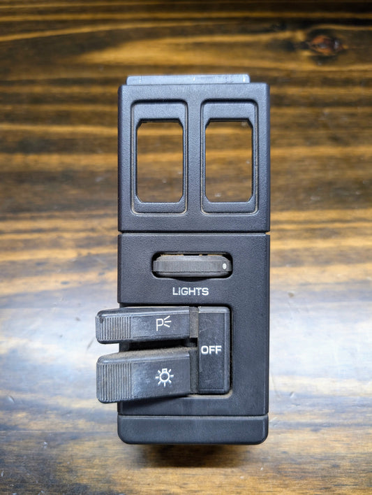 A close-up of a General Motors OEM Headlight Headlamp Switch in black for 1986-1994 Chevy S10, Blazer, GMC S15, and Jimmy, showing sliders with LIGHTS, OFF, parking and headlight symbols on a wooden surface.