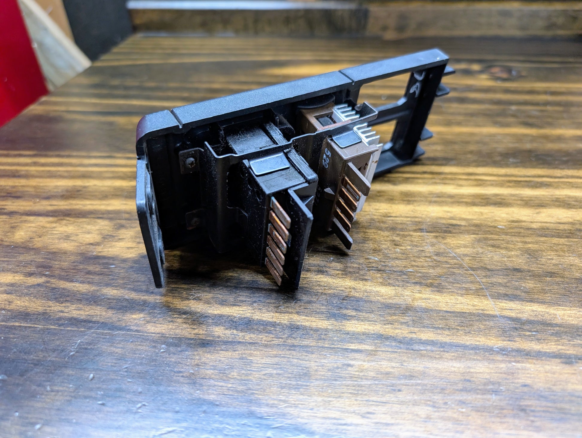 A close-up of a black OEM Headlight Headlamp Switch by General Motors for 1986–1994 Chevy S10, Blazer, GMC S15, and Jimmy. The device features exposed metallic pins and multiple slots, shown resting on a wooden surface.