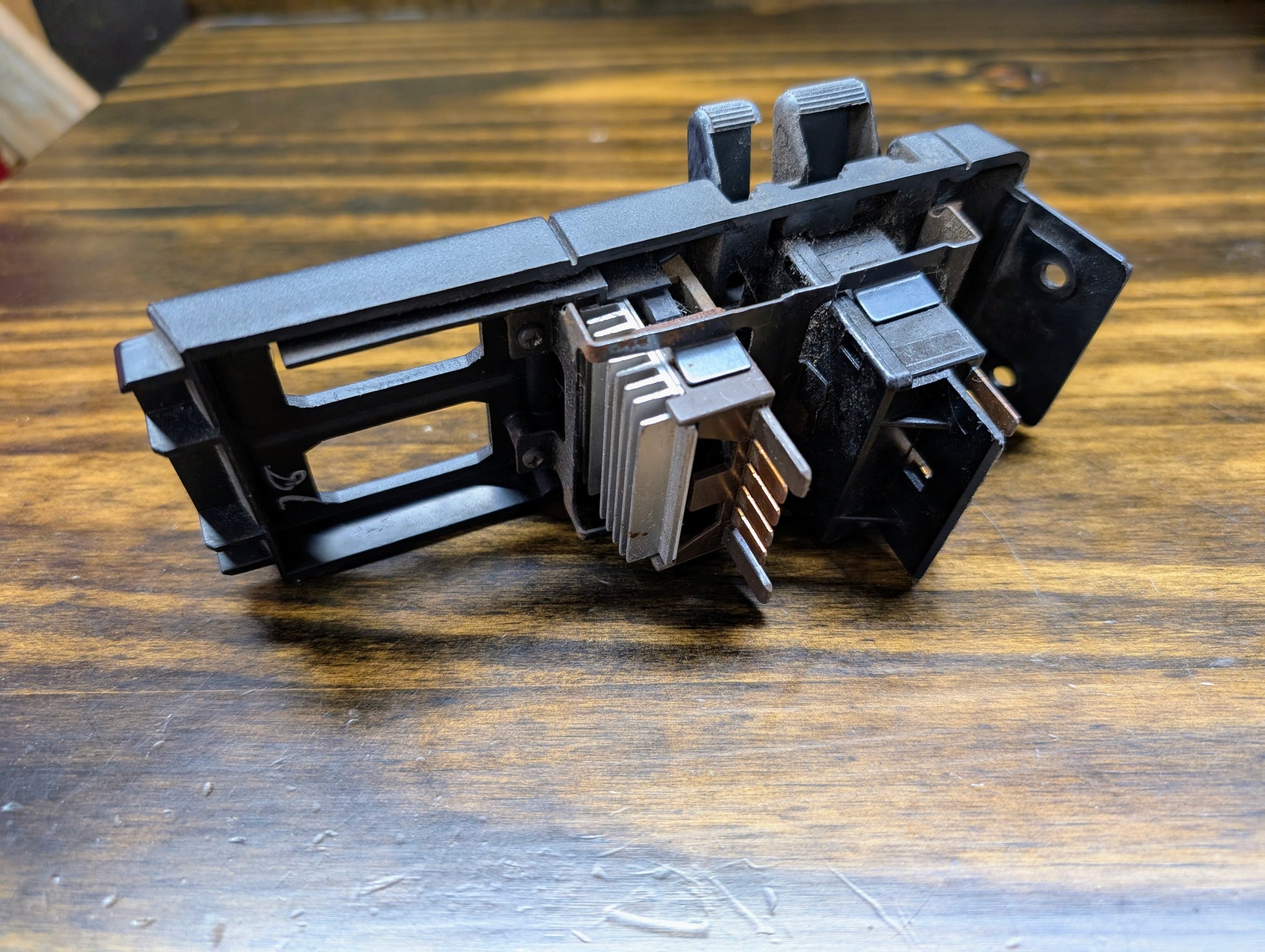 A black OEM Headlight Headlamp Switch by General Motors for 1986-1994 Chevy S10, Blazer, GMC S15, and Jimmy is shown on a wooden surface with visible metal fins and electrical connectors.