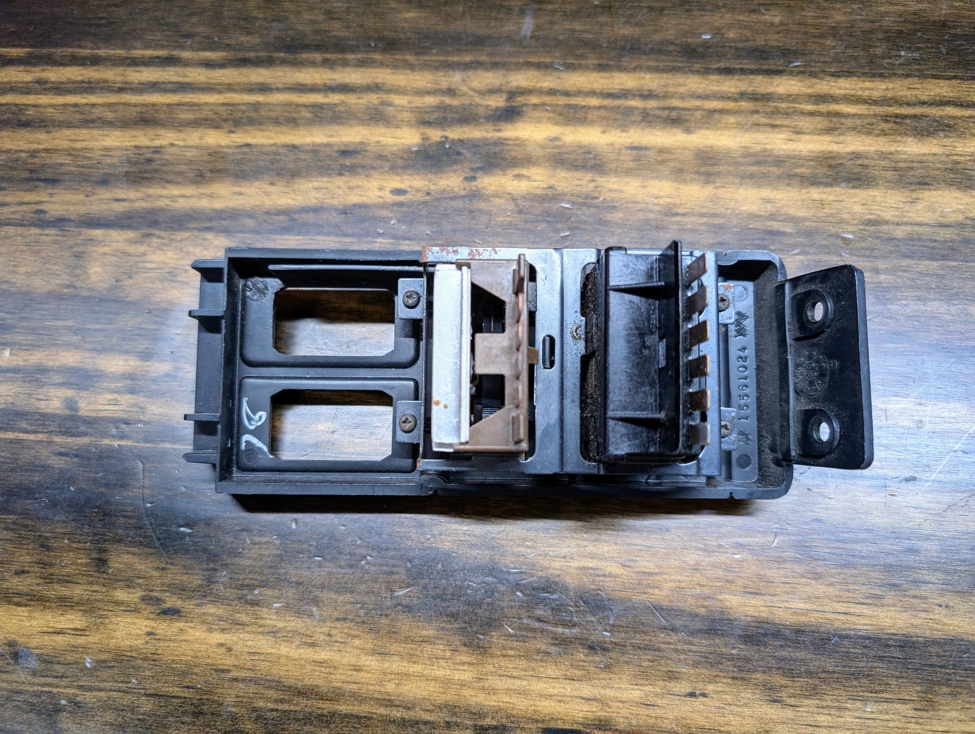 A used General Motors OEM Headlight Headlamp Switch in black for 1986-1994 Chevy S10, Blazer, GMC S15, and Jimmy is shown on a wooden surface, displaying visible wear, slight rust, and multiple connection slots.