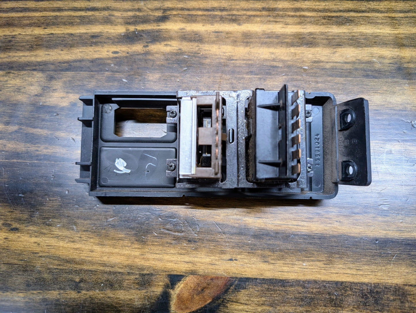 A close-up of a black OEM Headlight Headlamp Switch by General Motors for 1986-1994 Chevy S10, Blazer, GMC S15, and Jimmy, featuring connectors and slots, resting on a wooden surface with visible grain.