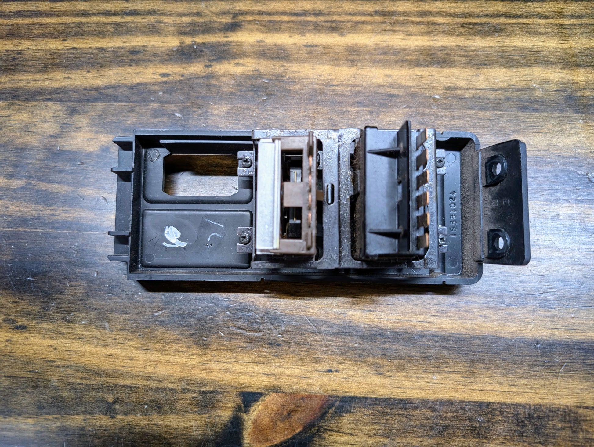 A close-up of a black OEM Headlight Headlamp Switch by General Motors for 1986-1994 Chevy S10, Blazer, GMC S15, and Jimmy, featuring connectors and slots, resting on a wooden surface with visible grain.