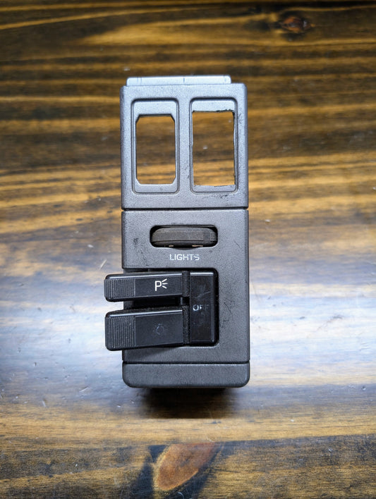 A black OEM General Motors headlight switch for 1986-1994 Chevy S10, Blazer, GMC S15, and Jimmy features two levers marked P and OFF. Ideal replacement part labeled LIGHTS. Shown on a wooden surface.