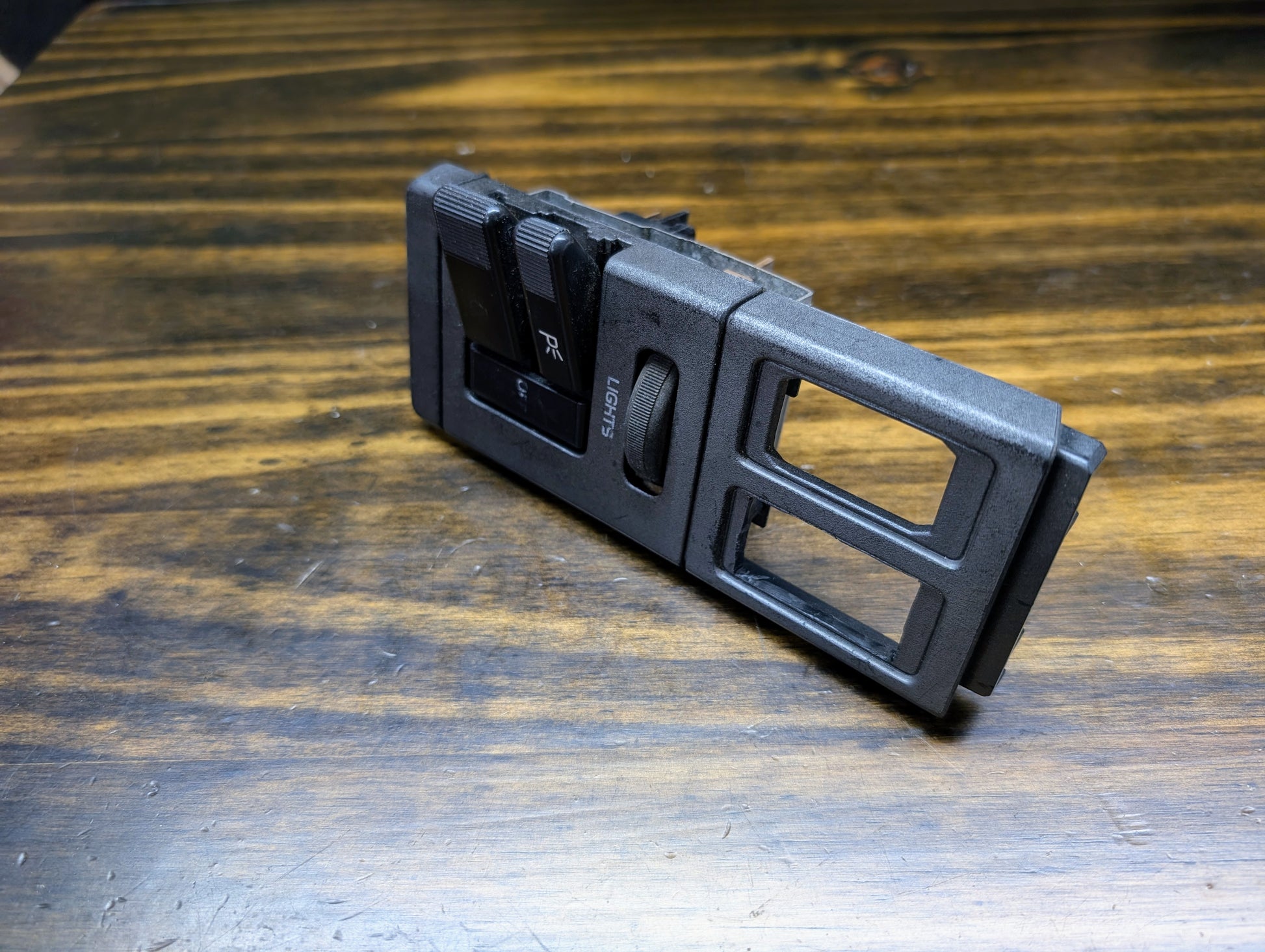 A General Motors OEM Headlight Headlamp Switch for 1986–1994 Chevy S10, Blazer, GMC S15, and Jimmy is shown angled on a wooden surface, emphasizing its buttons and slots.