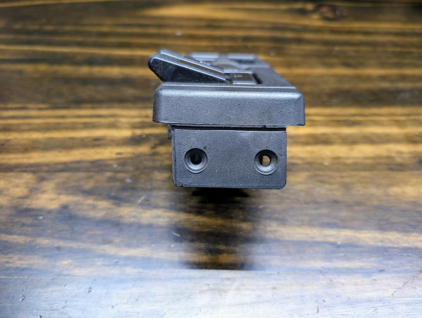 Close-up of a General Motors OEM Headlight Switch for 1986-1994 Chevy S10, Blazer, GMC S15, and Jimmy, featuring two round holes and a lever, shown on a wooden surface with visible grain.