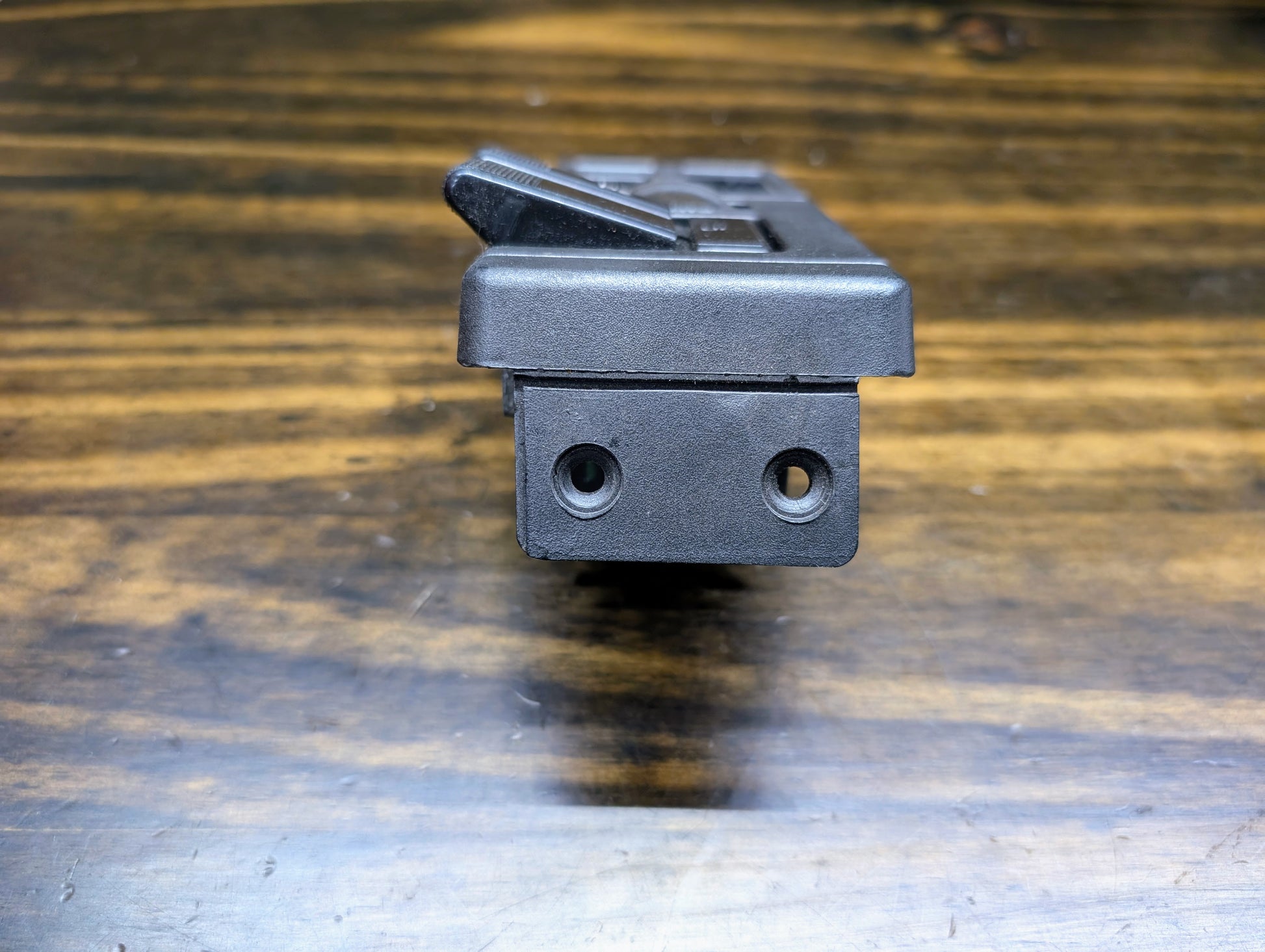 Close-up of a General Motors OEM Headlight Switch for 1986-1994 Chevy S10, Blazer, GMC S15, and Jimmy, featuring two round holes and a lever, shown on a wooden surface with visible grain.