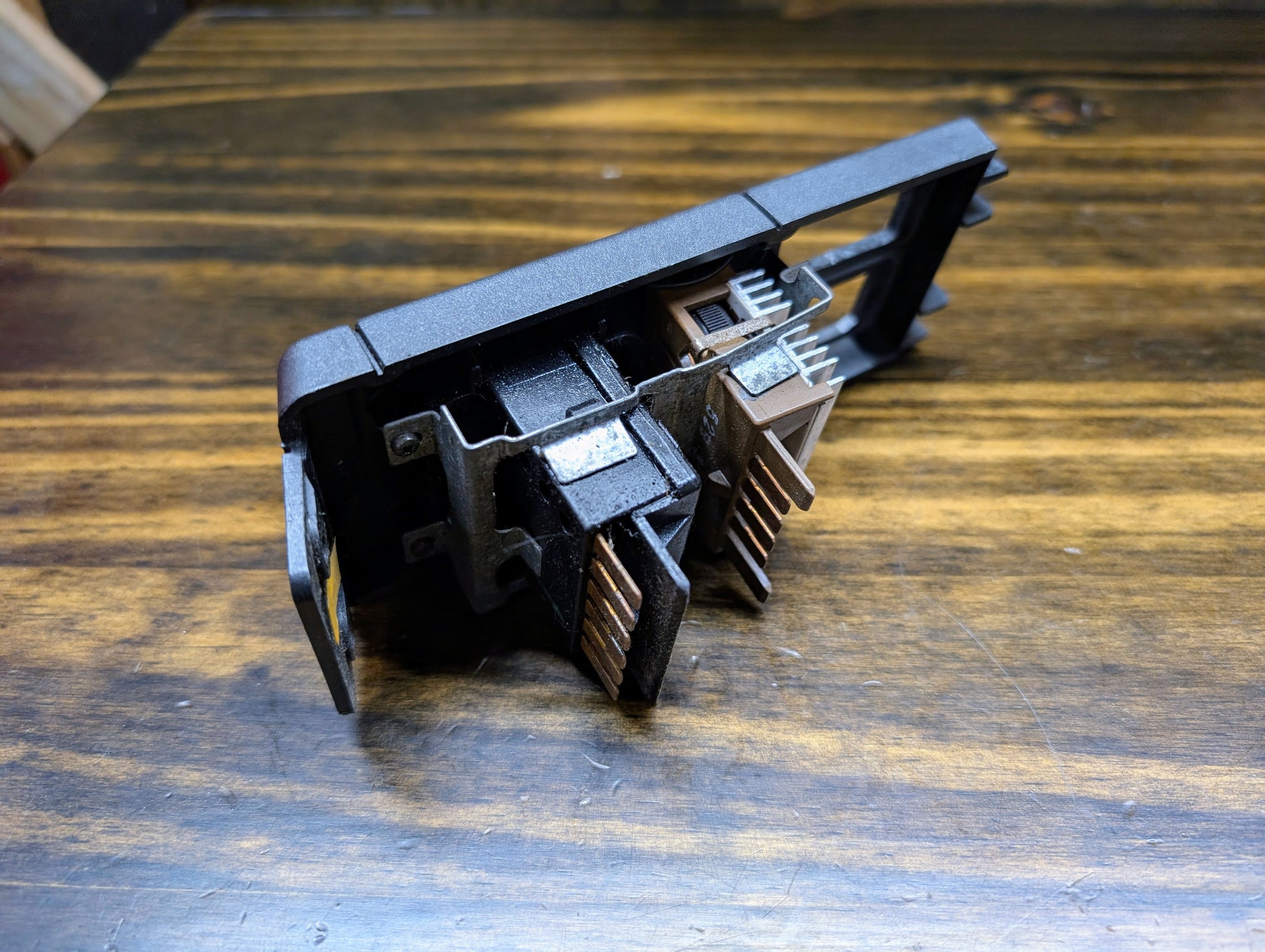 A close-up of a General Motors OEM Headlight Headlamp Switch for 1986-1994 Chevy S10, Blazer, GMC S15, and Jimmy shows its metal connectors and black plastic housing resting on a wood-grain surface.